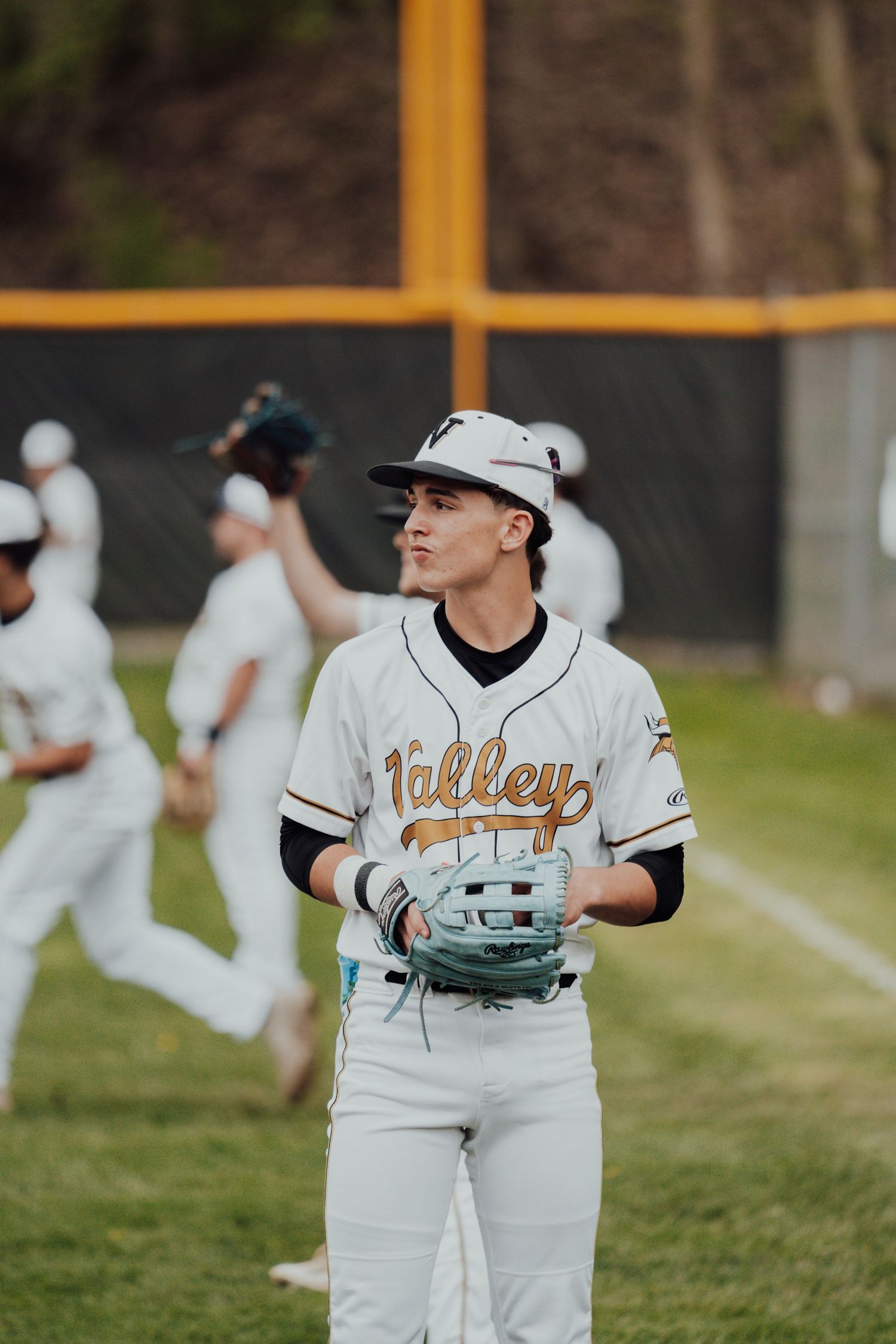Baseball player in white Valley uniform holds glove on field during game practice.