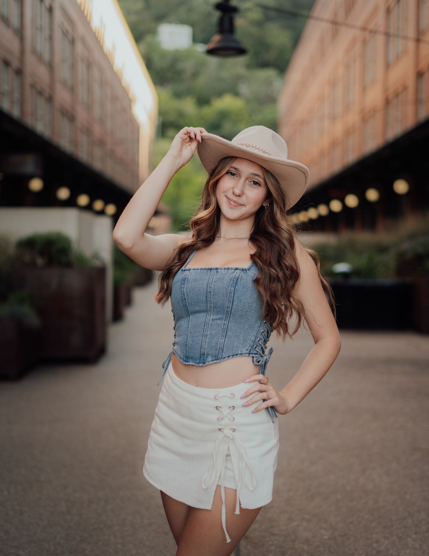 A person in a wide-brimmed hat and denim top poses confidently in an urban tunnel setting with warm lighting.