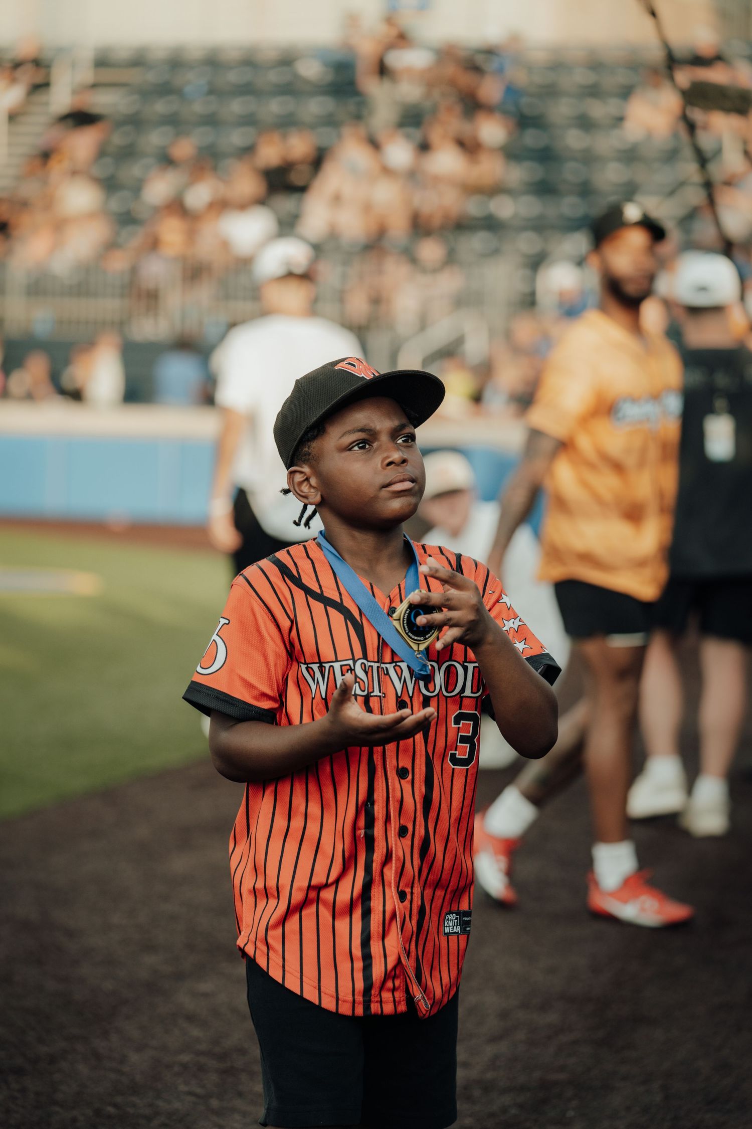 A player in an orange and black striped baseball uniform stands ready with hands raised and a focused expression.