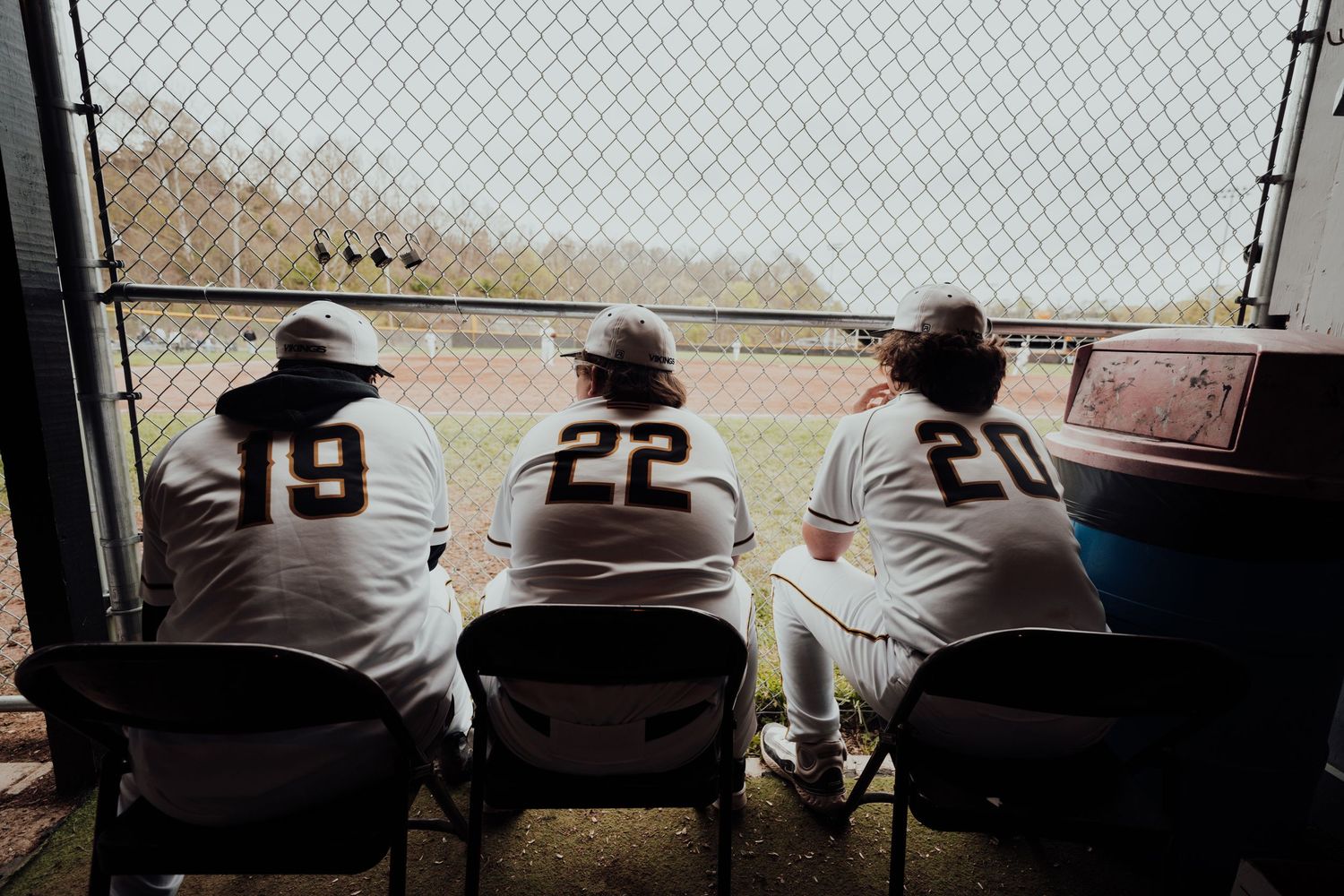 Baseball players watch the game from the dugout bench.