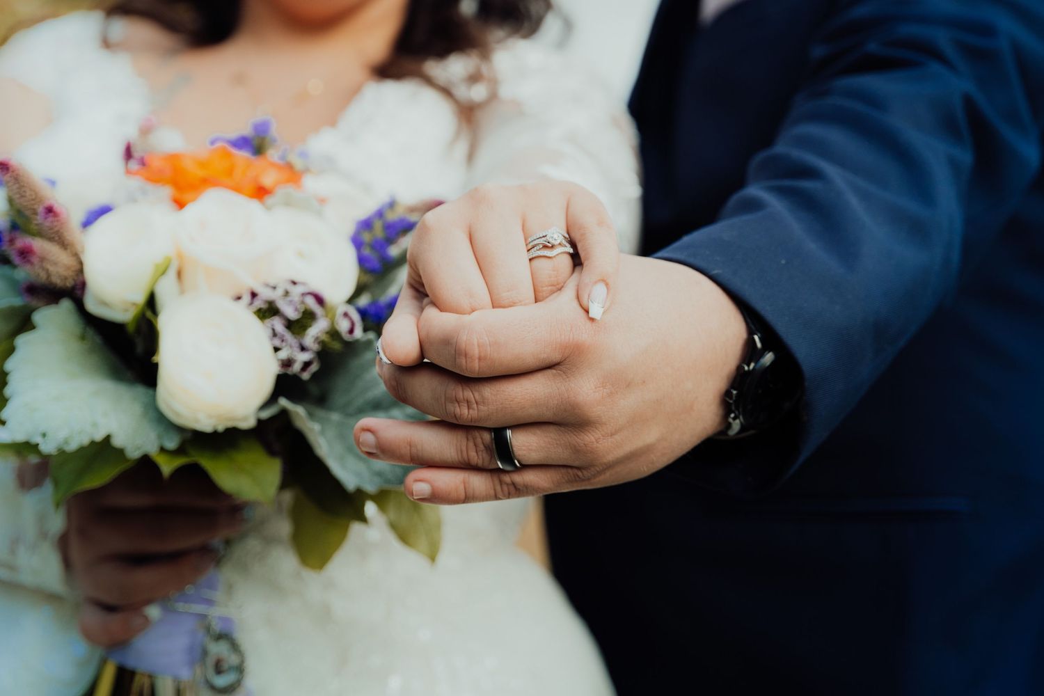 Close-up of hands holding delicate wedding bouquet with purple and white flowers.