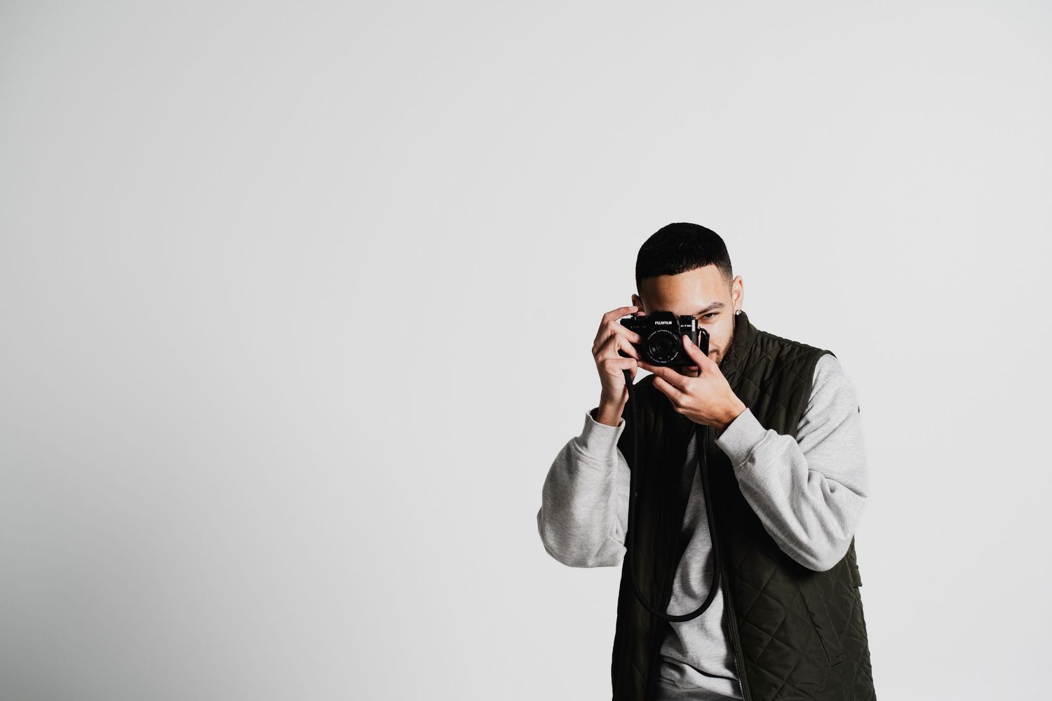 Photographer in casual attire holding a vintage camera against white background.
