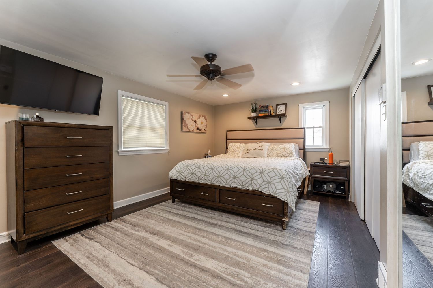 Modern bedroom with dark wood furniture, light gray walls, hardwood floors, and a ceiling fan.