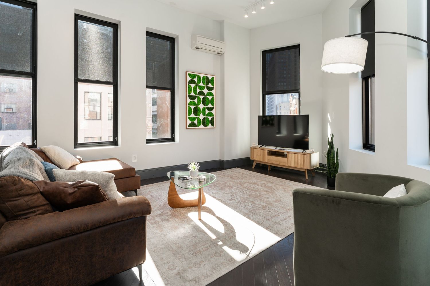 Modern minimalist living room with brown sofa, white walls, and large windows letting in natural light.