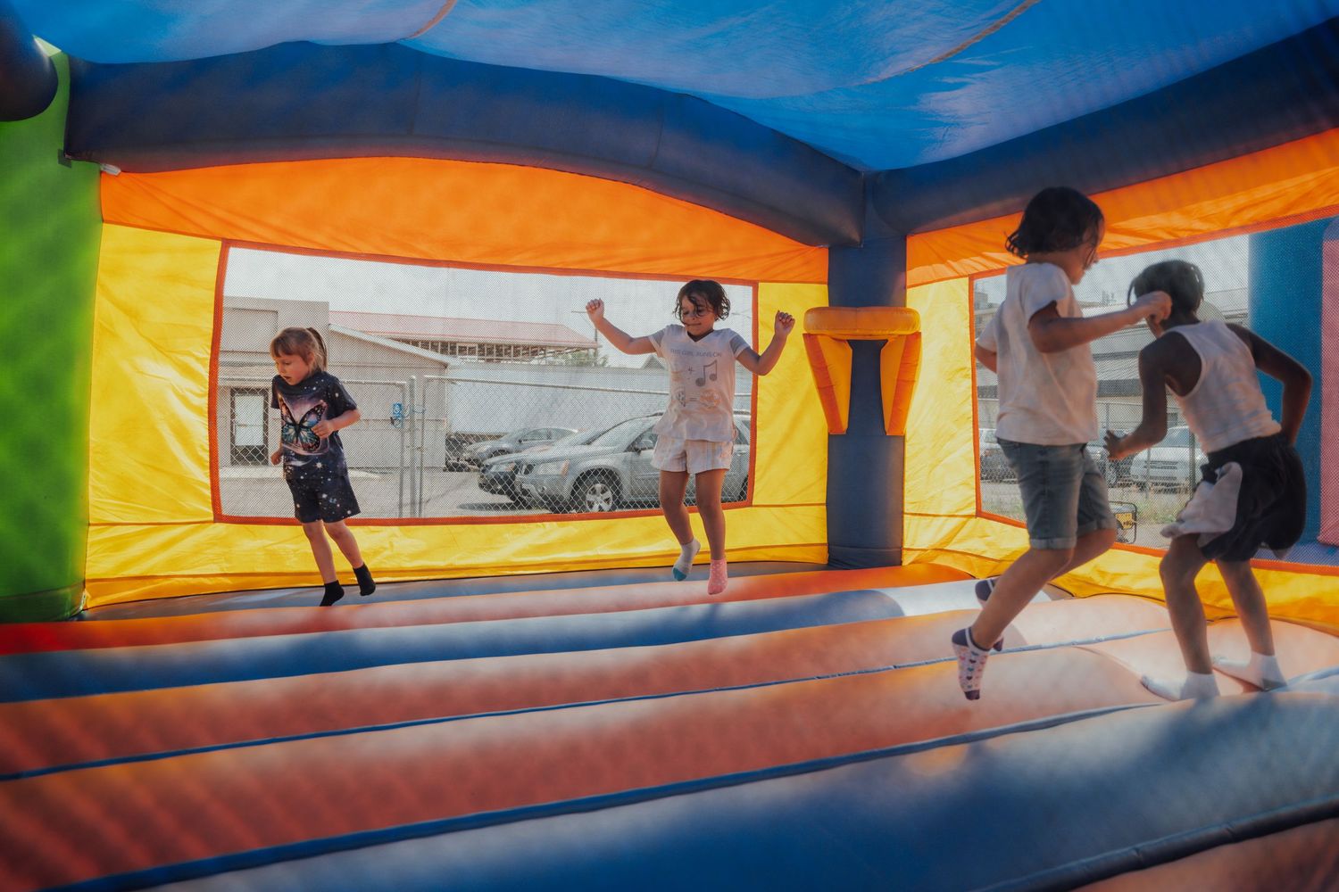 People having fun bouncing and playing in a colorful inflatable bounce house under blue and orange fabric.