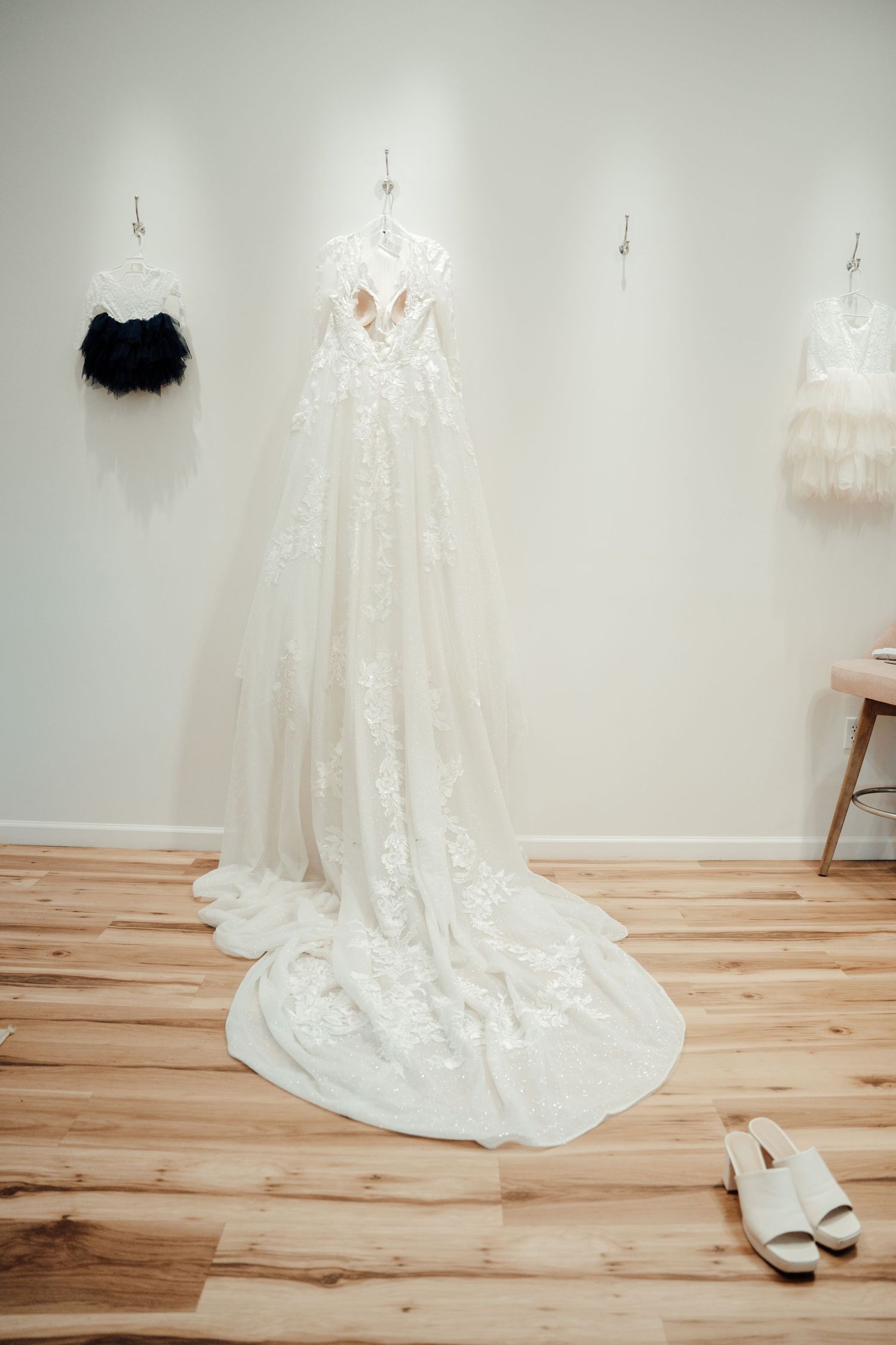 Elegant white lace wedding dress hanging on display with black and cream accessories.
