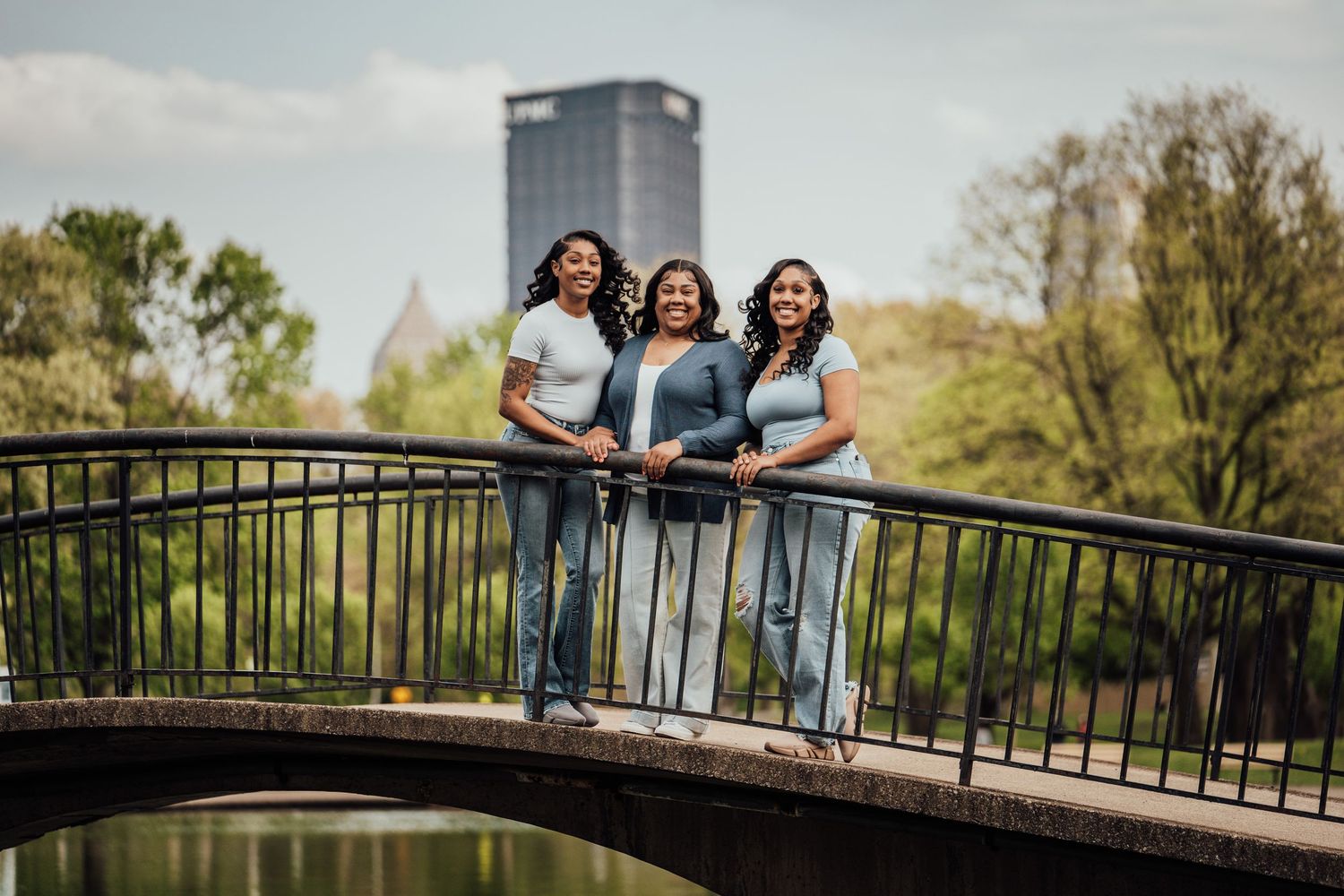 Group enjoys candid laughter while sitting on a scenic bridge railing during outdoor photography session in natural setting.