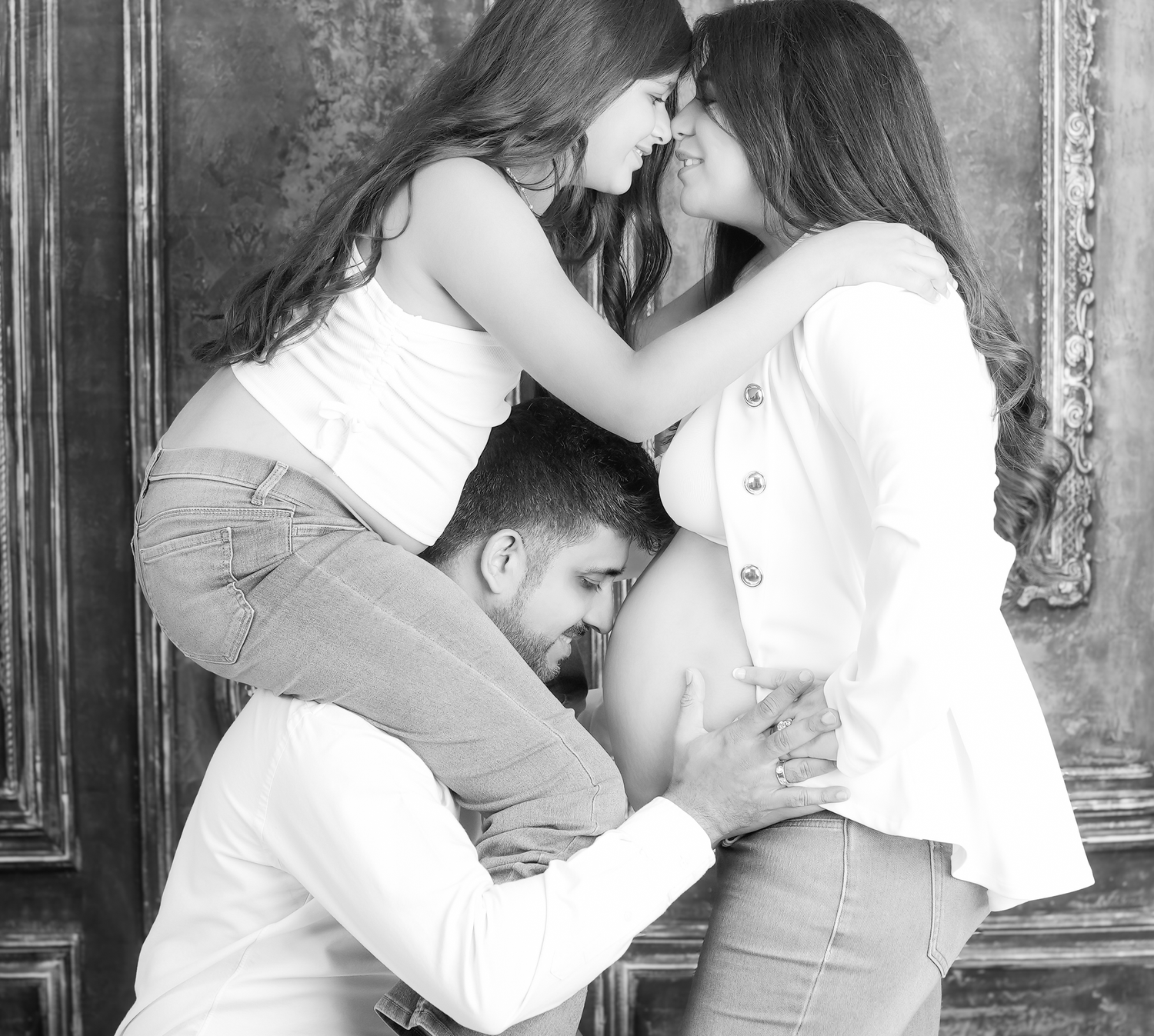 Black and white intimate photograph showing tender closeness and affection between three people in a loving embrace.