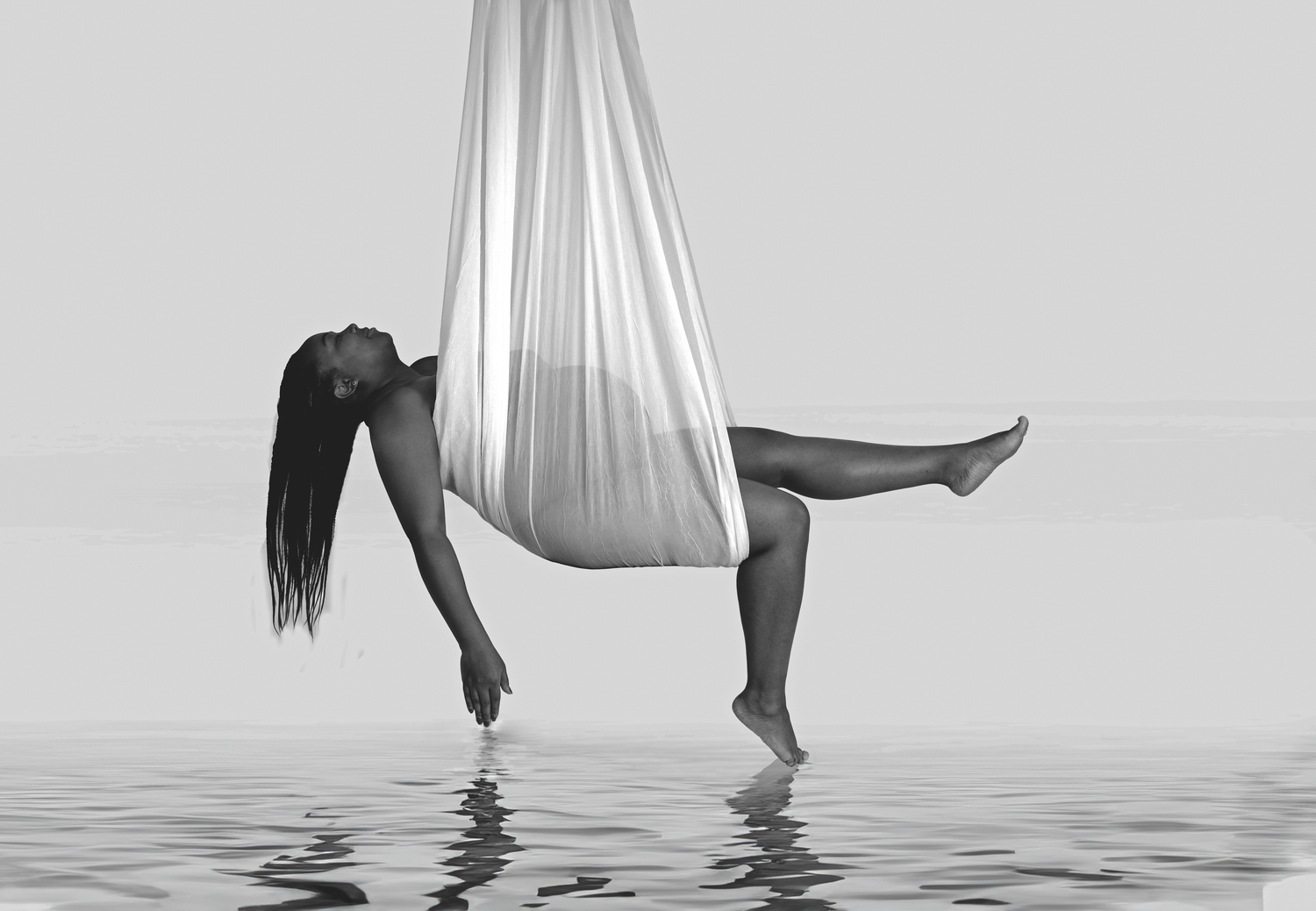 An artistic black and white photo series shows feet dangling from floating white fabric in a reflective pool of water.