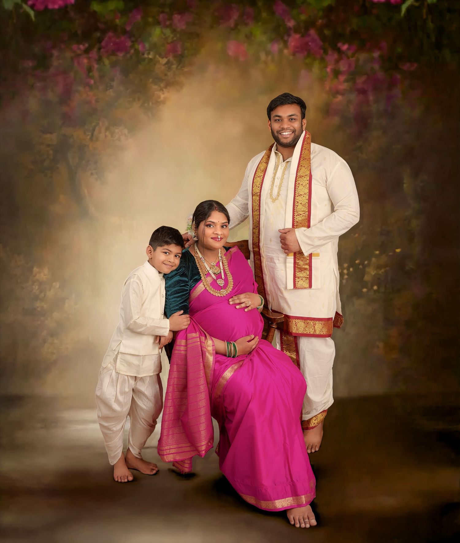 A traditional south Indian family poses together in formal attire against a dreamy backdrop with pink flowers.