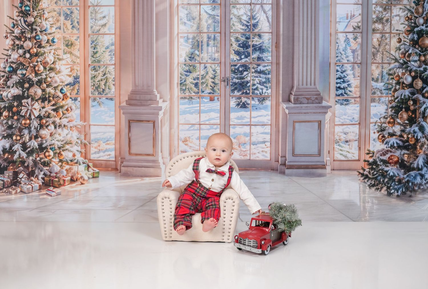 Decorated holiday scene with small chair and vintage red truck toy beside Christmas trees in an elegant setting.