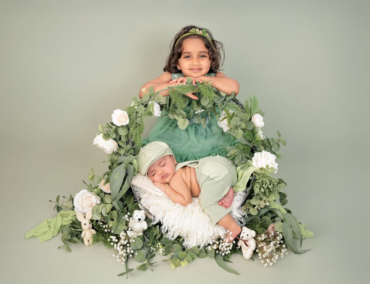 Newborn baby sleeps peacefully surrounded by delicate white flowers and soft green foliage in dreamy studio setting.