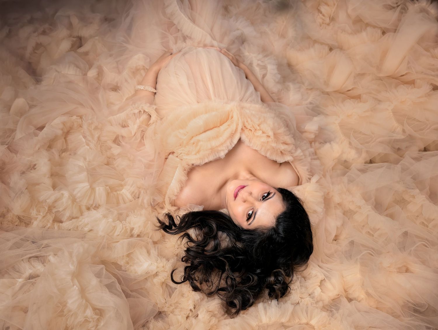 Aerial view of someone lying on textured peach-colored tulle fabric with dark curly hair spread out.