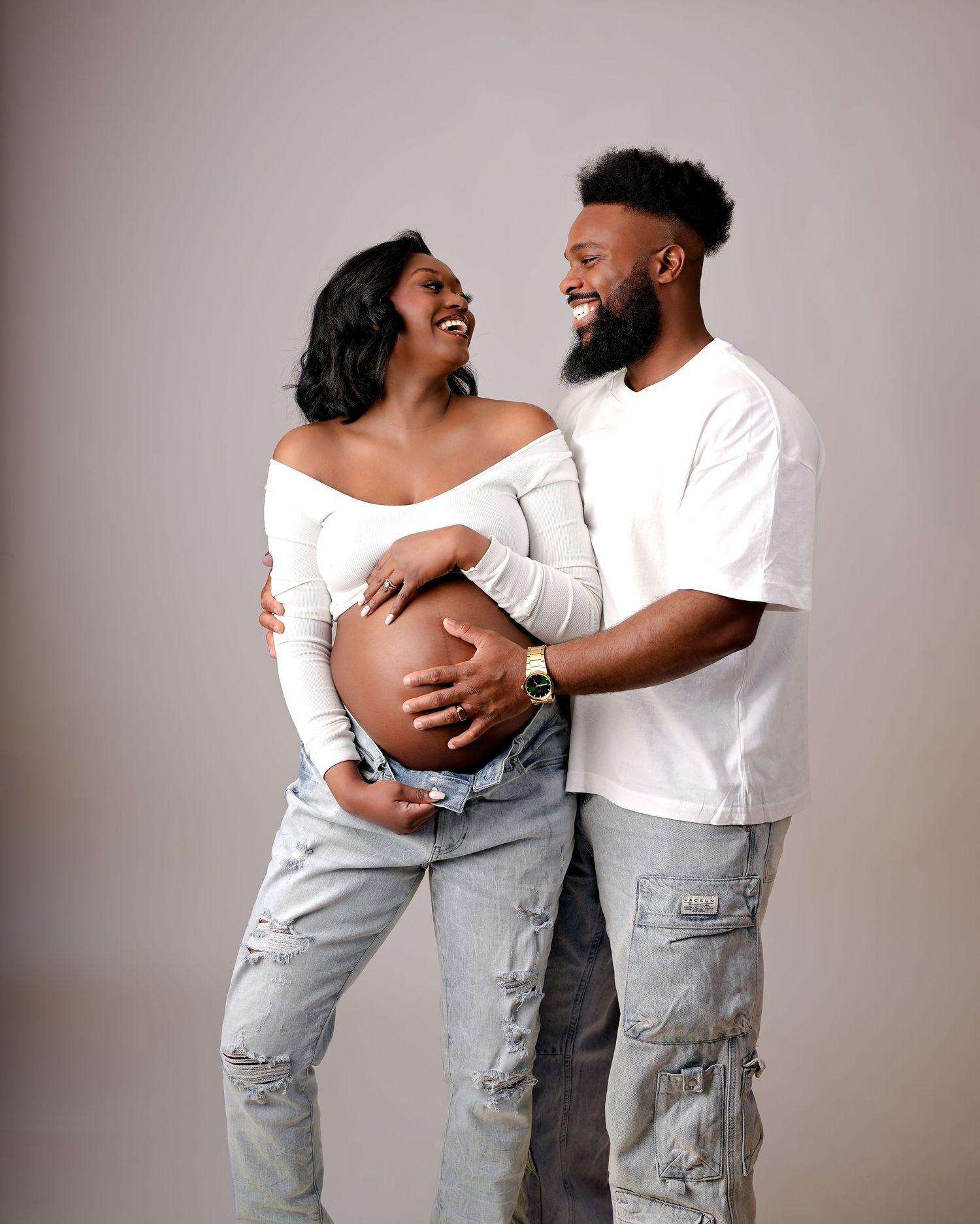 A loving couple embraces and laughs joyfully together while wearing white shirts and distressed denim in a portrait series.