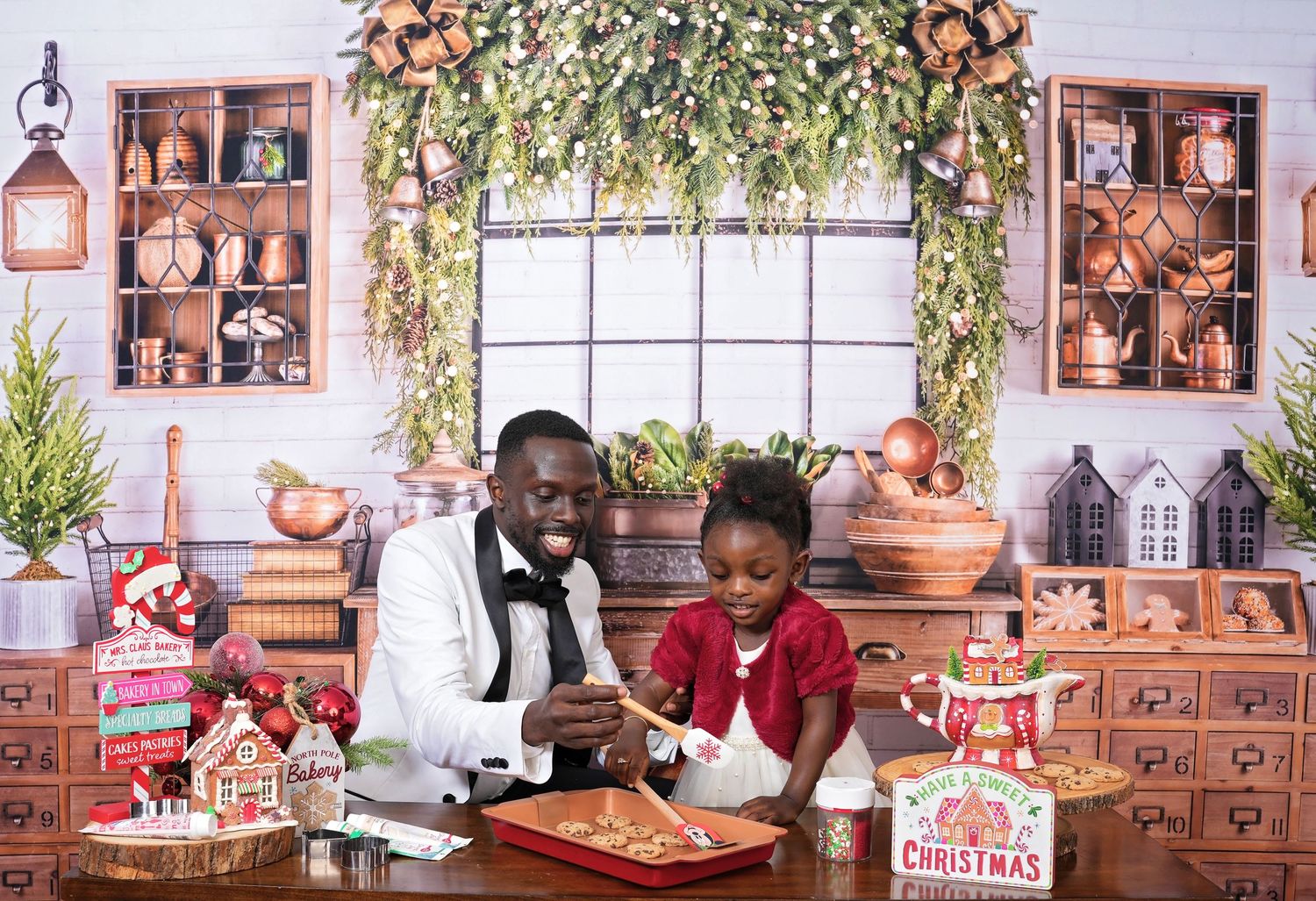 Two people decorate gingerbread cookies together at a festive holiday baking station with rustic decor and garland.