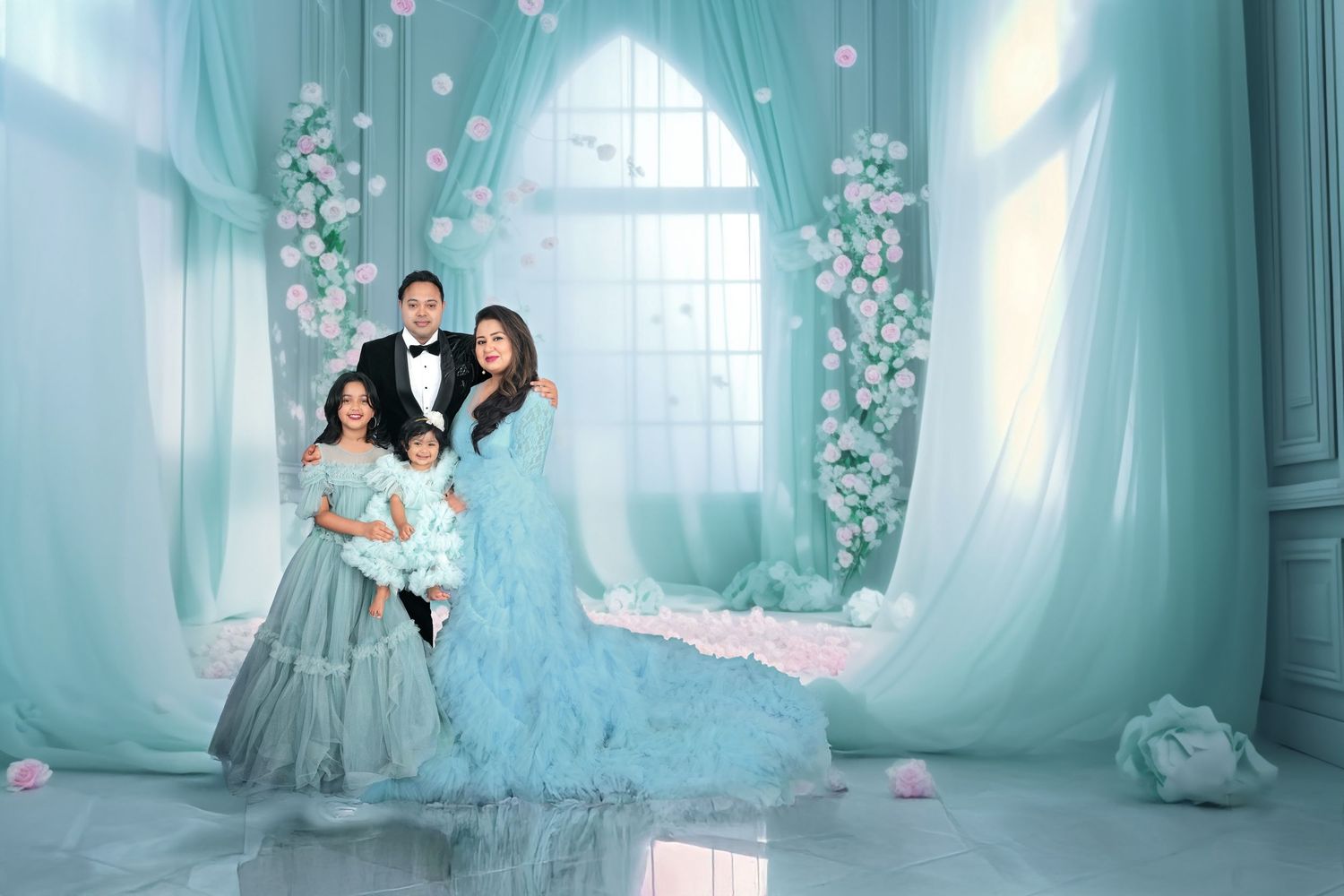 Elegant family portrait in a dreamy turquoise studio setting with arched windows and floral decorations.