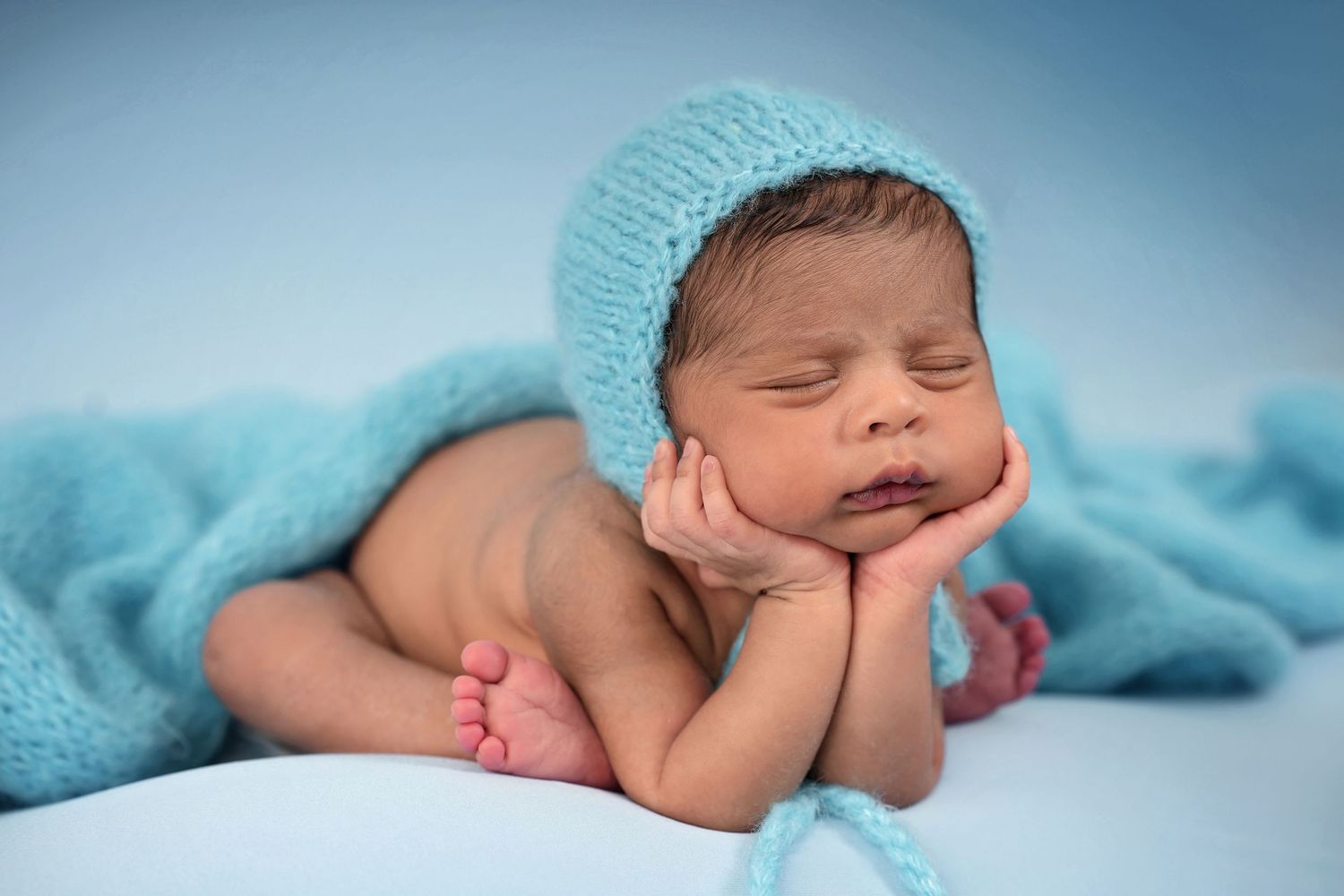 Sleeping newborn baby wrapped in soft turquoise blanket during professional photoshoot.