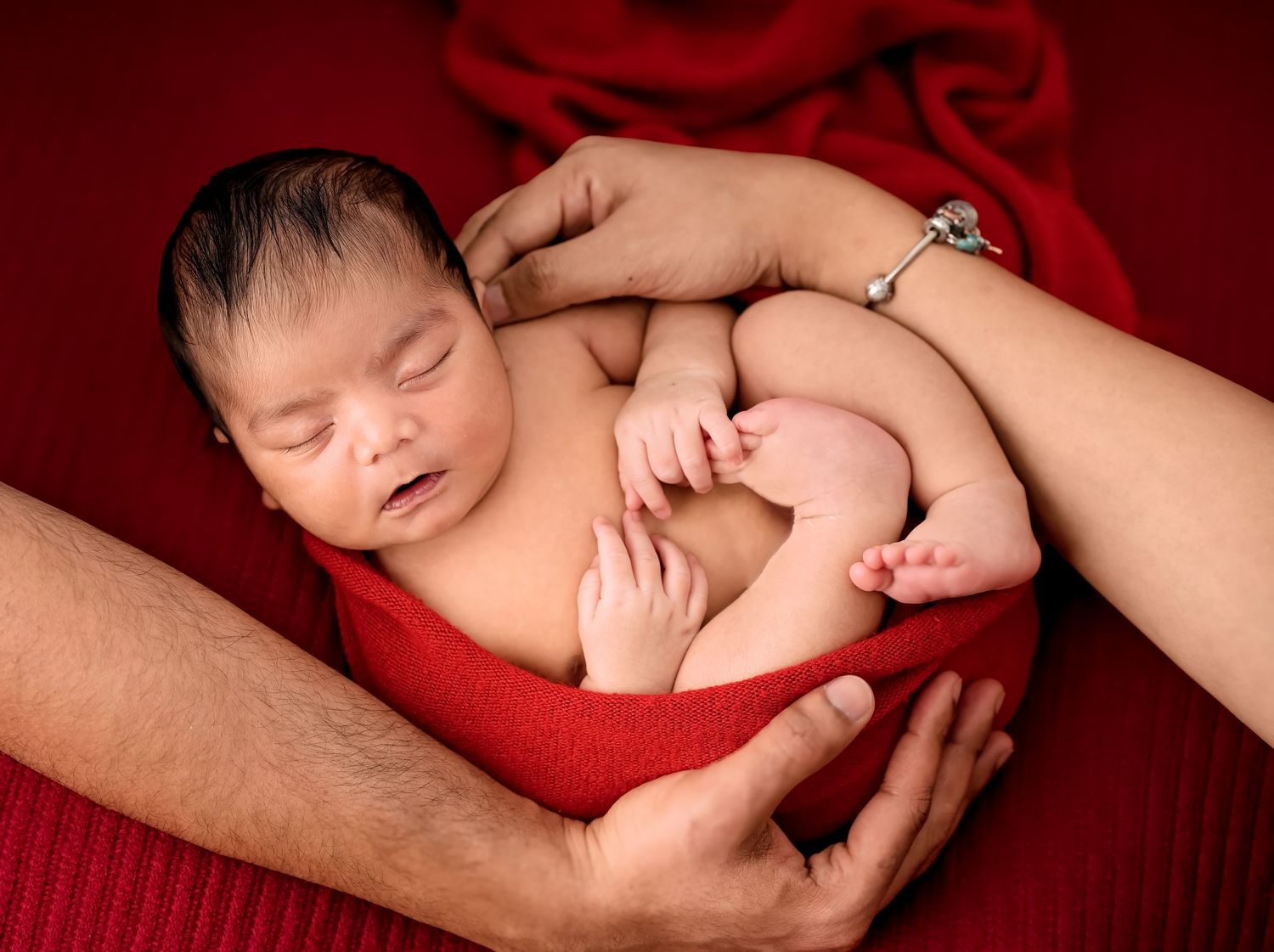 Newborn baby sleeping tranquilly on red velvet blankets in multiple poses during professional photo session.
