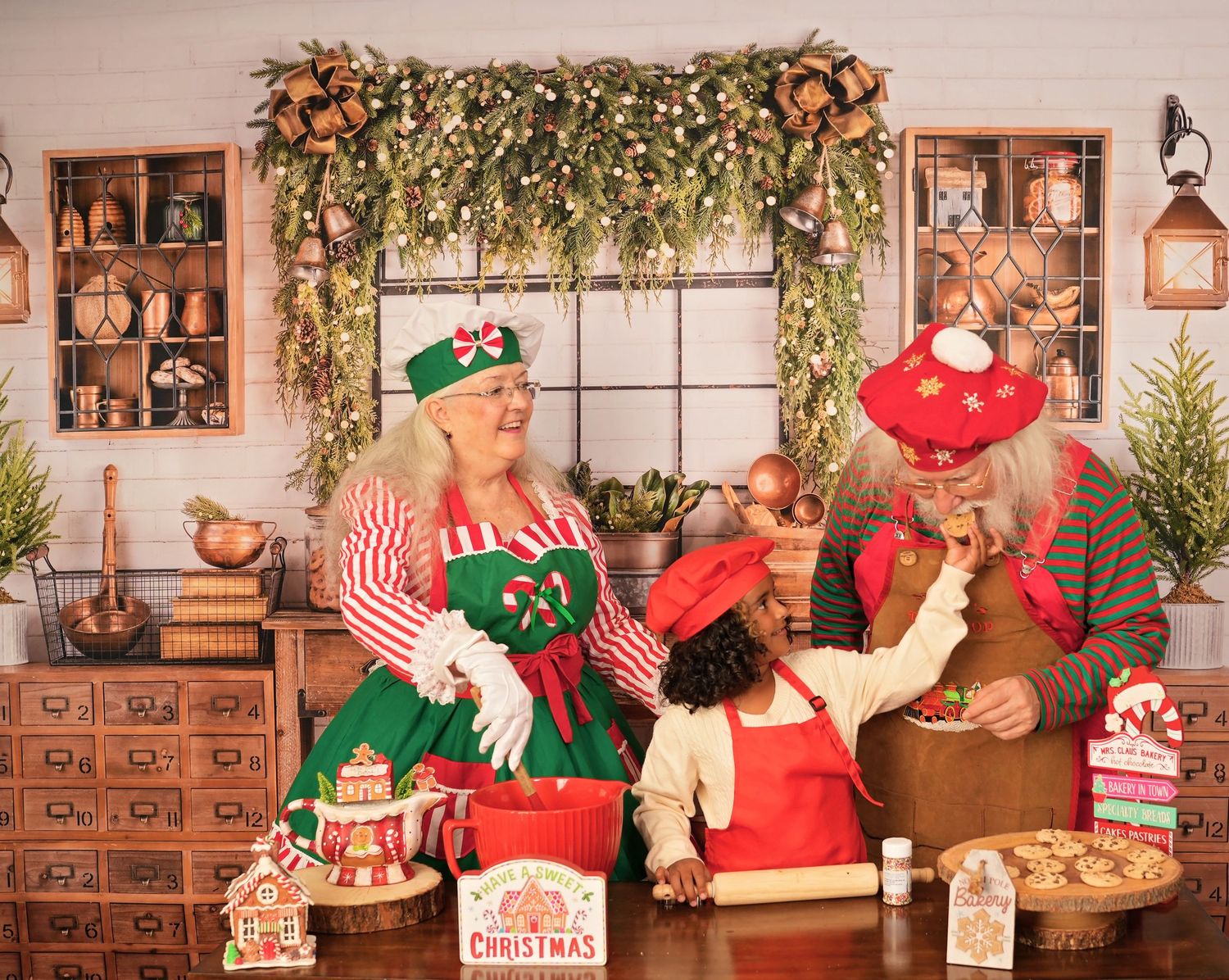 Mrs. Claus and an elf bake Christmas cookies together in a festive holiday kitchen decorated with garland and seasonal decor.
