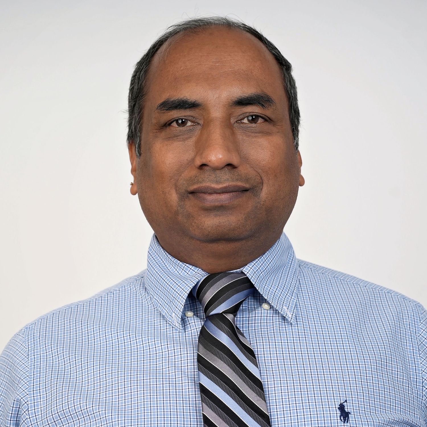 Professional headshot portrait of someone wearing a light blue button-down shirt and striped tie against white background.