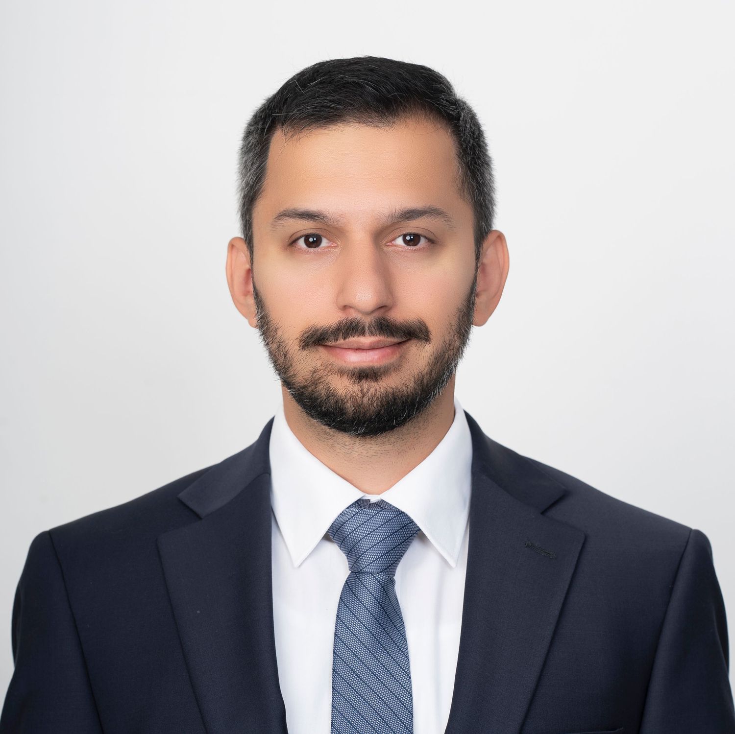 Professional headshot of person in dark suit and blue tie against white background.