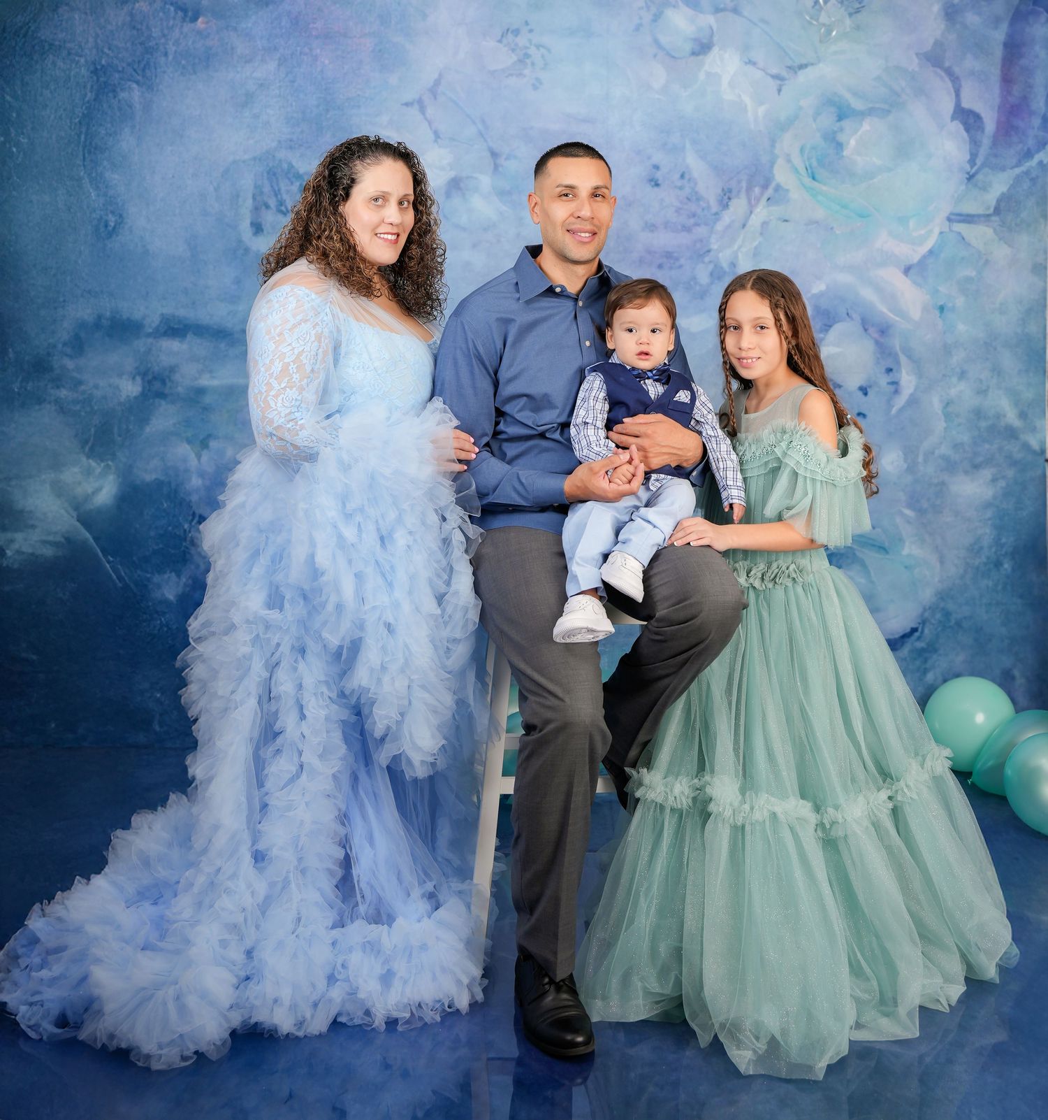 Family portrait session against blue backdrop featuring coordinated mint green and gray formal attire.