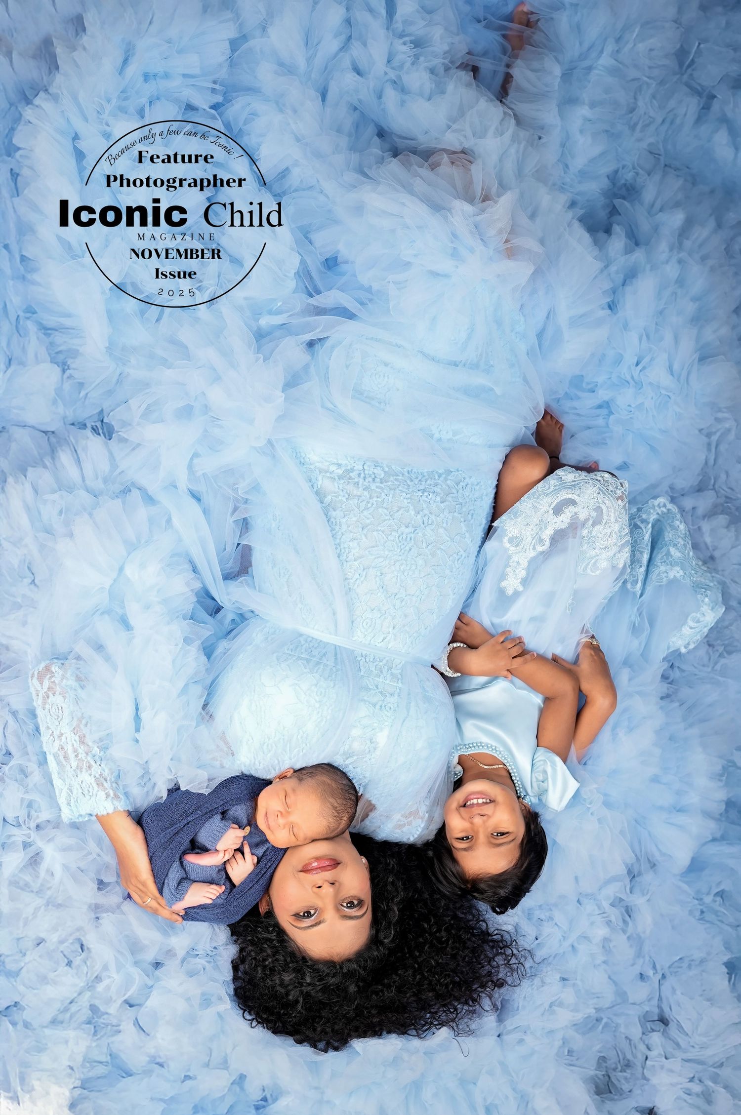 Mother and daughter in light blue dresses lying down with newborn baby, featured in Iconic Child Magazine November issue.