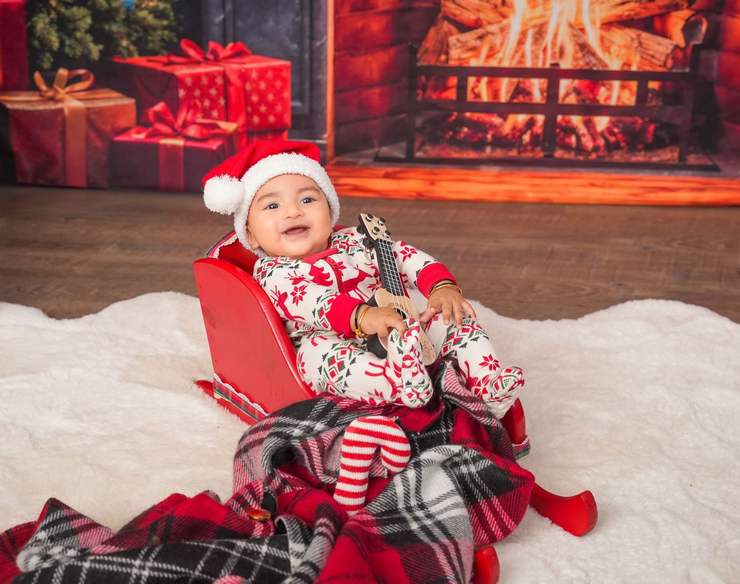 Cozy winter scene with holiday decorations, plaid blankets and a red sleigh in front of a glowing fireplace.