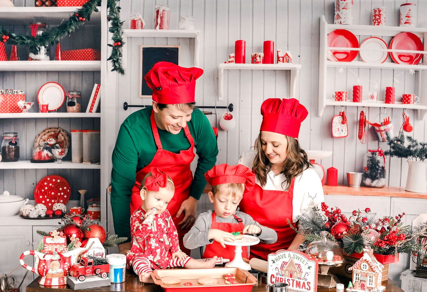 Family in red chef hats and aprons baking Christmas cookies together in a festive holiday kitchen.