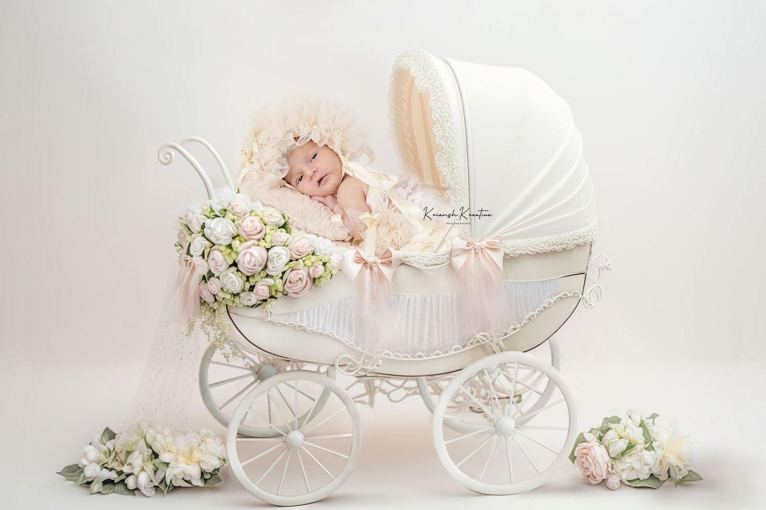 A vintage white baby carriage decorated with pink roses and delicate floral arrangements creates an elegant nursery display.