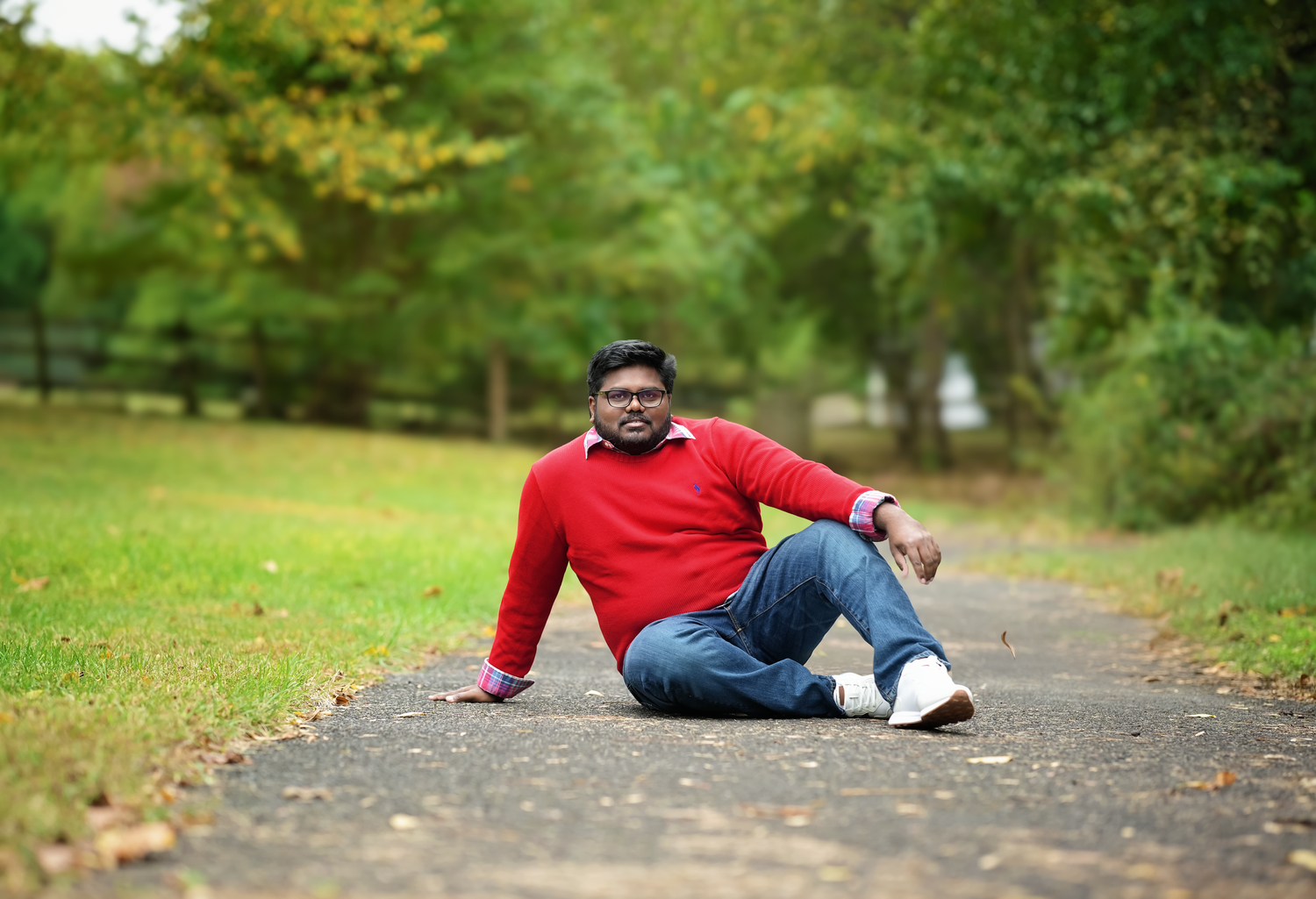 A person in a red sweater sits on a fallen autumn leaf-covered path in a park.