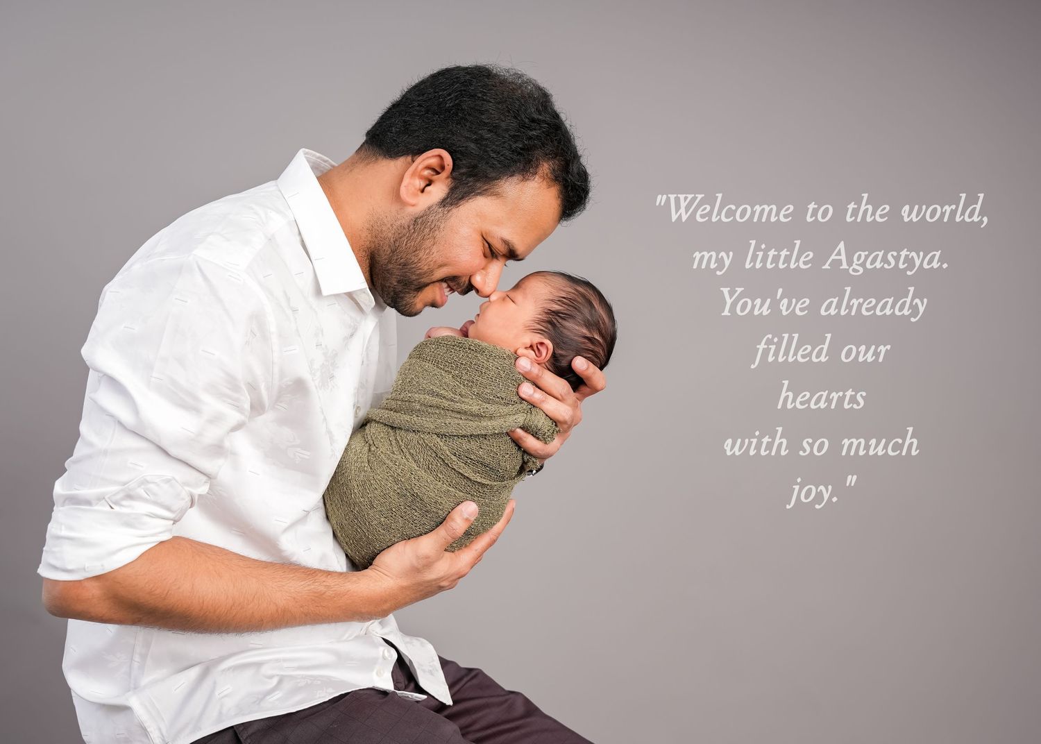 Parent cradles newborn baby lovingly while standing in soft neutral lighting against a beige wall.