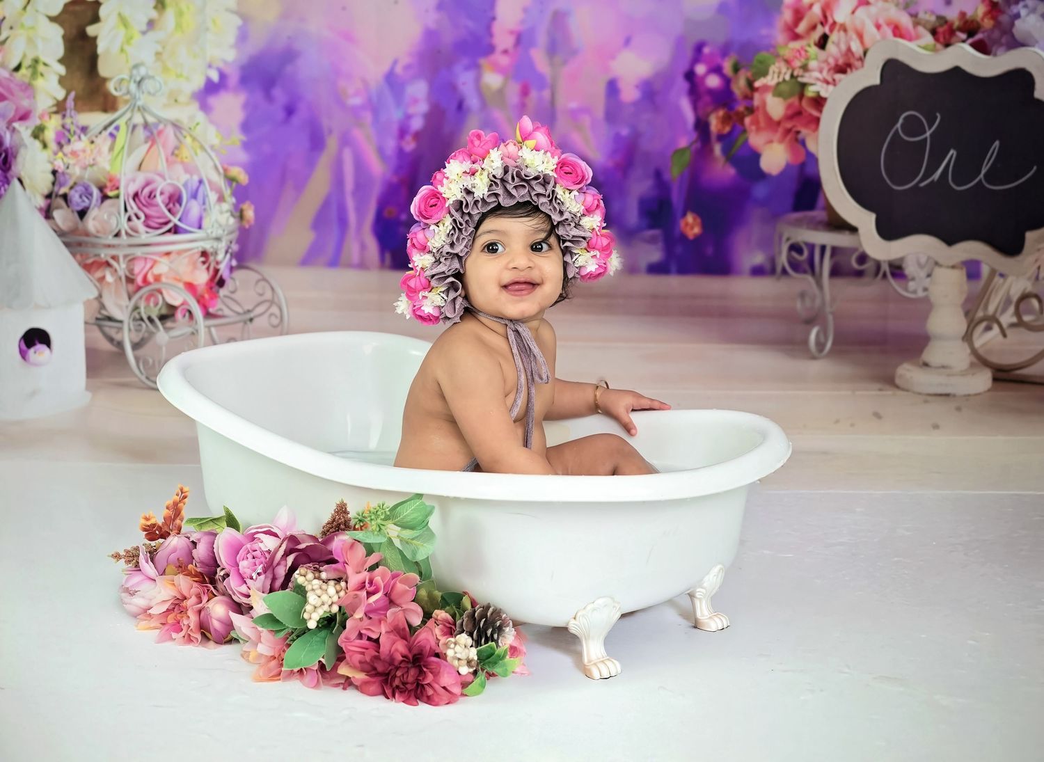 Beautiful floral milk bath photography setup with vintage white clawfoot tub surrounded by pink flowers and purple lighting.