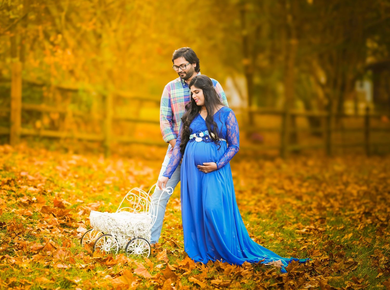 A couple in a bright blue dress and suit embrace among vibrant autumn leaves in a romantic outdoor setting.