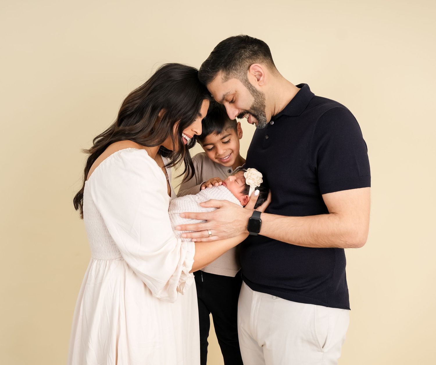 A loving family moment as parents cuddle their newborn baby against a beige backdrop.