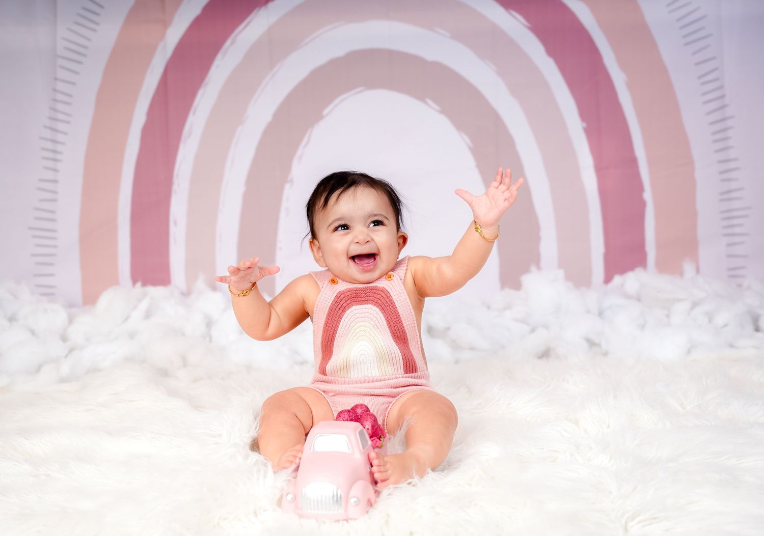 A smiling baby in a pink tutu outfit sitting on a light gray backdrop with multiple reflective images around them.