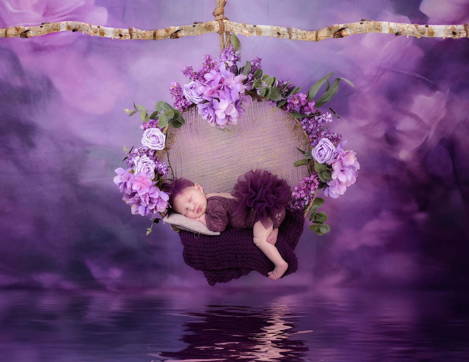 Floral wreath swing with purple roses and greenery suspended over reflective water with purple ethereal backdrop.