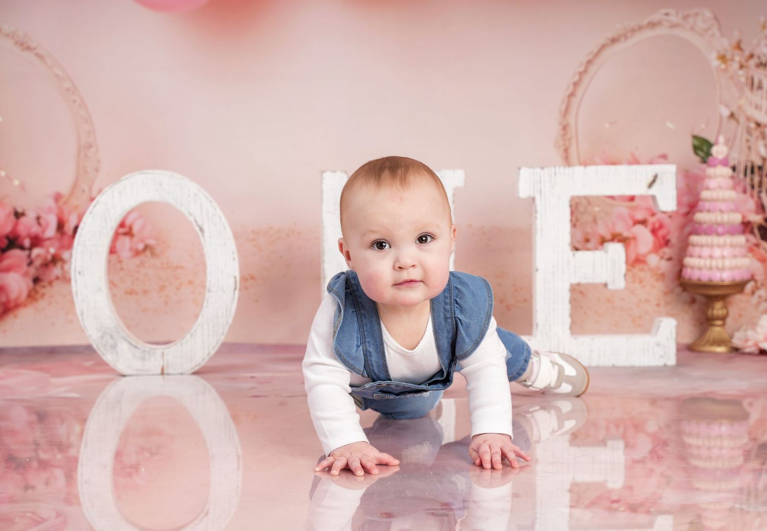 Baby crawling on pink and white floral backdrop during professional photo session.