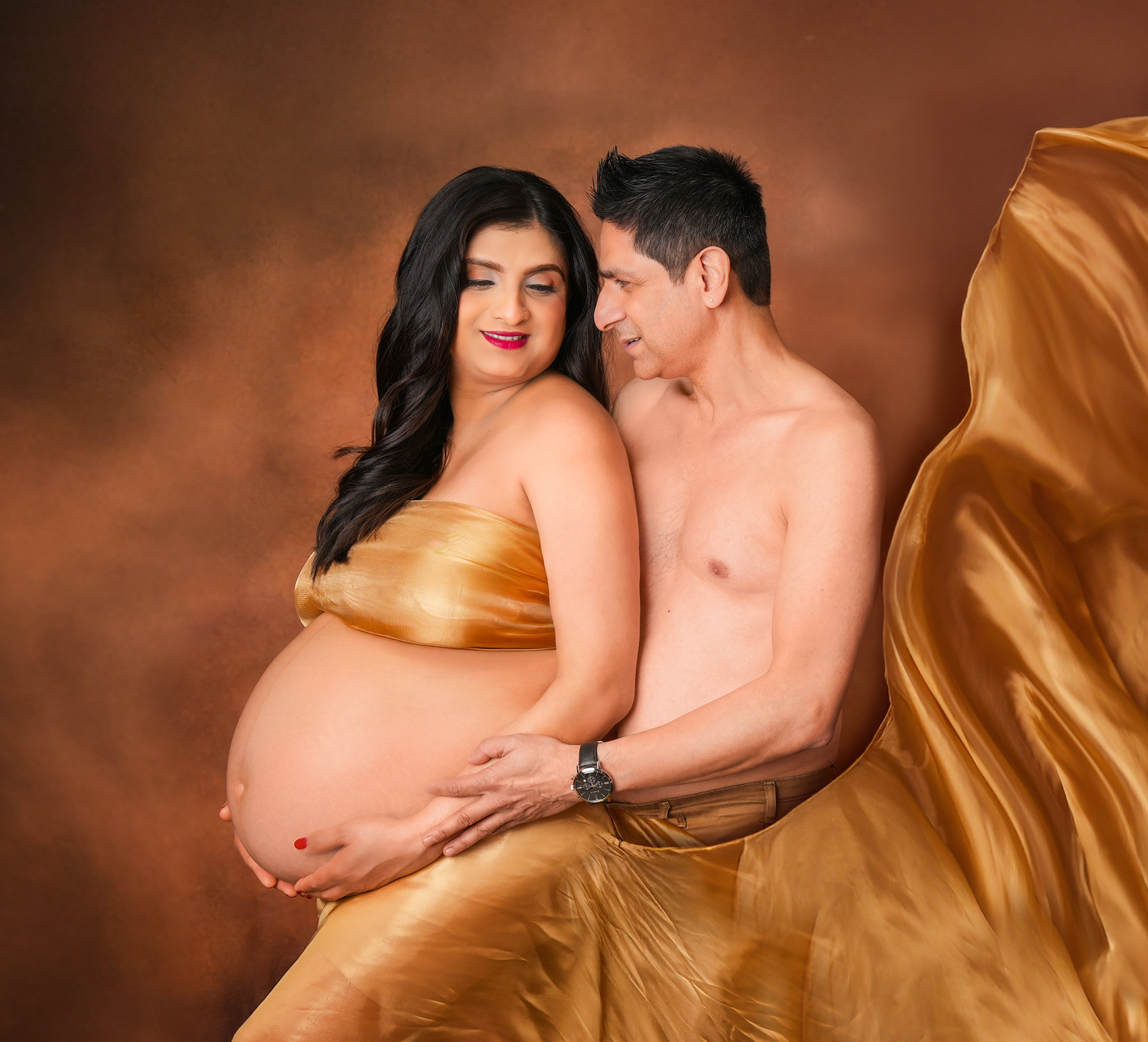 Artistic maternity photo series showing a woman in flowing gold fabric against a warm brown background.