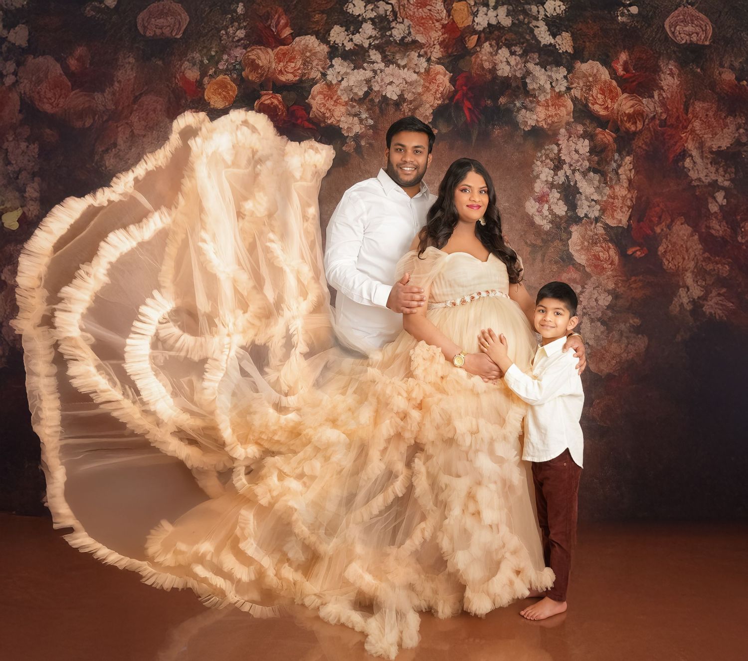 Beautiful maternity photo featuring a flowy champagne gown against a dark floral backdrop.