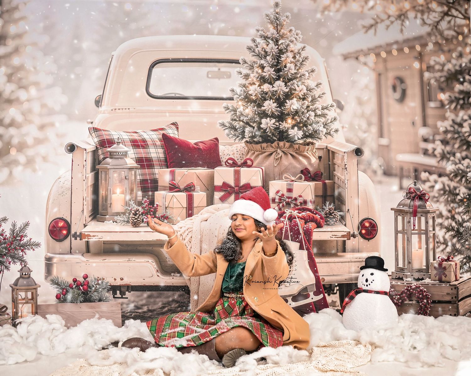 Child in Santa hat sits by vintage white truck with Christmas gifts, snowman, and snowy trees in festive holiday scene.