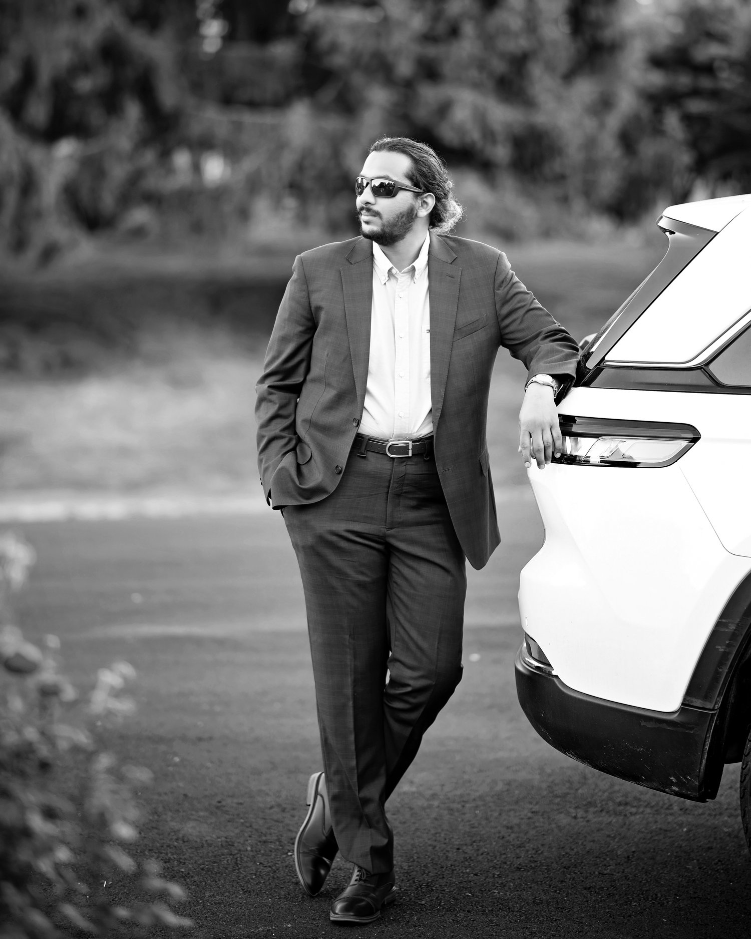 Professional in a dark suit walks confidently across a grassy field while carrying a briefcase in black and white.