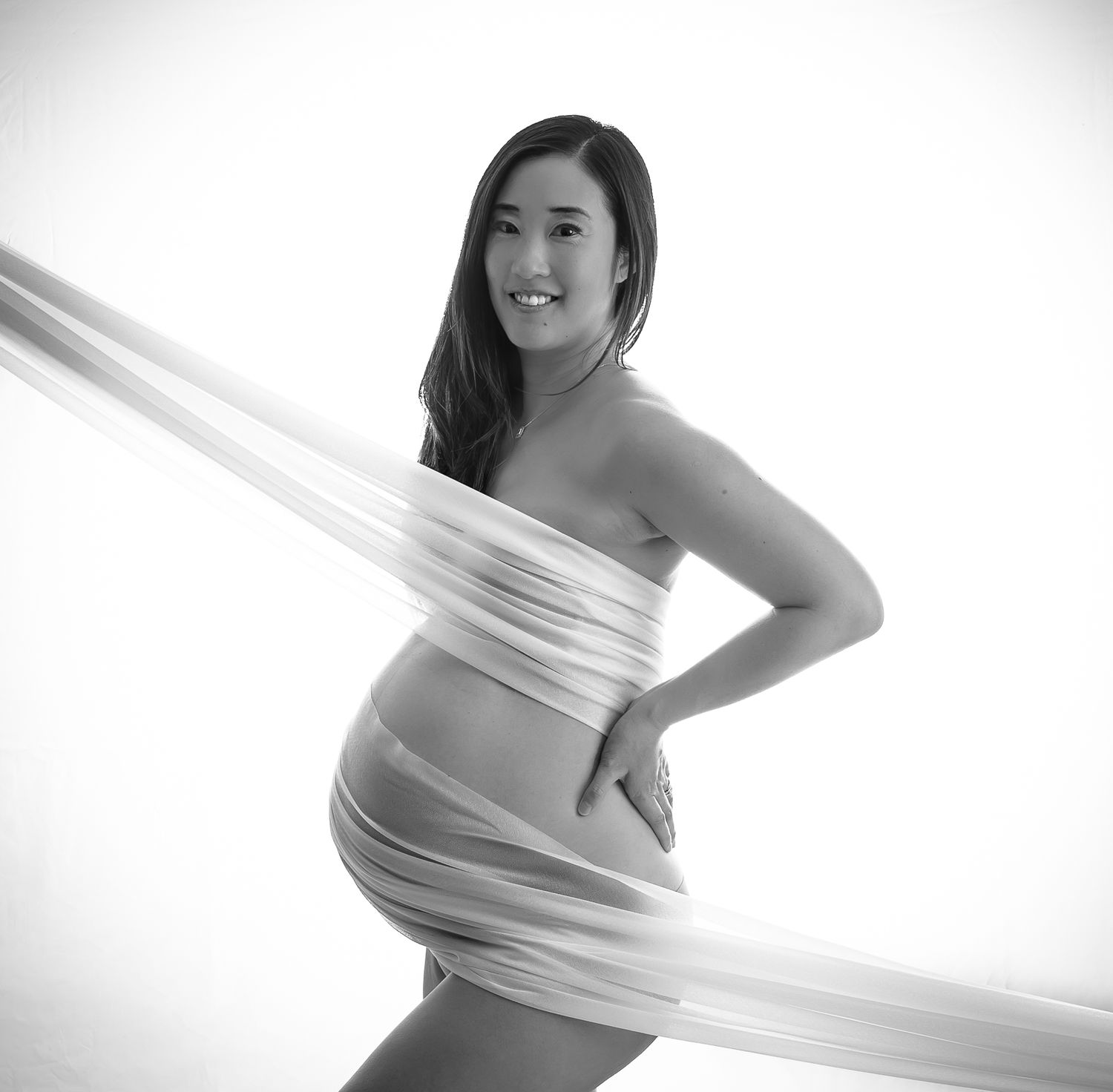 A black and white maternity photo session featuring artistic silhouette poses wrapped in flowing fabric.