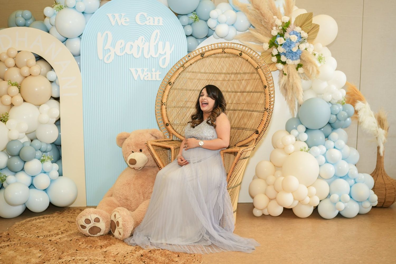 Baby shower celebration with elegant balloon arches in blue and white featuring a wicker peacock chair and dreamy decor setup.
