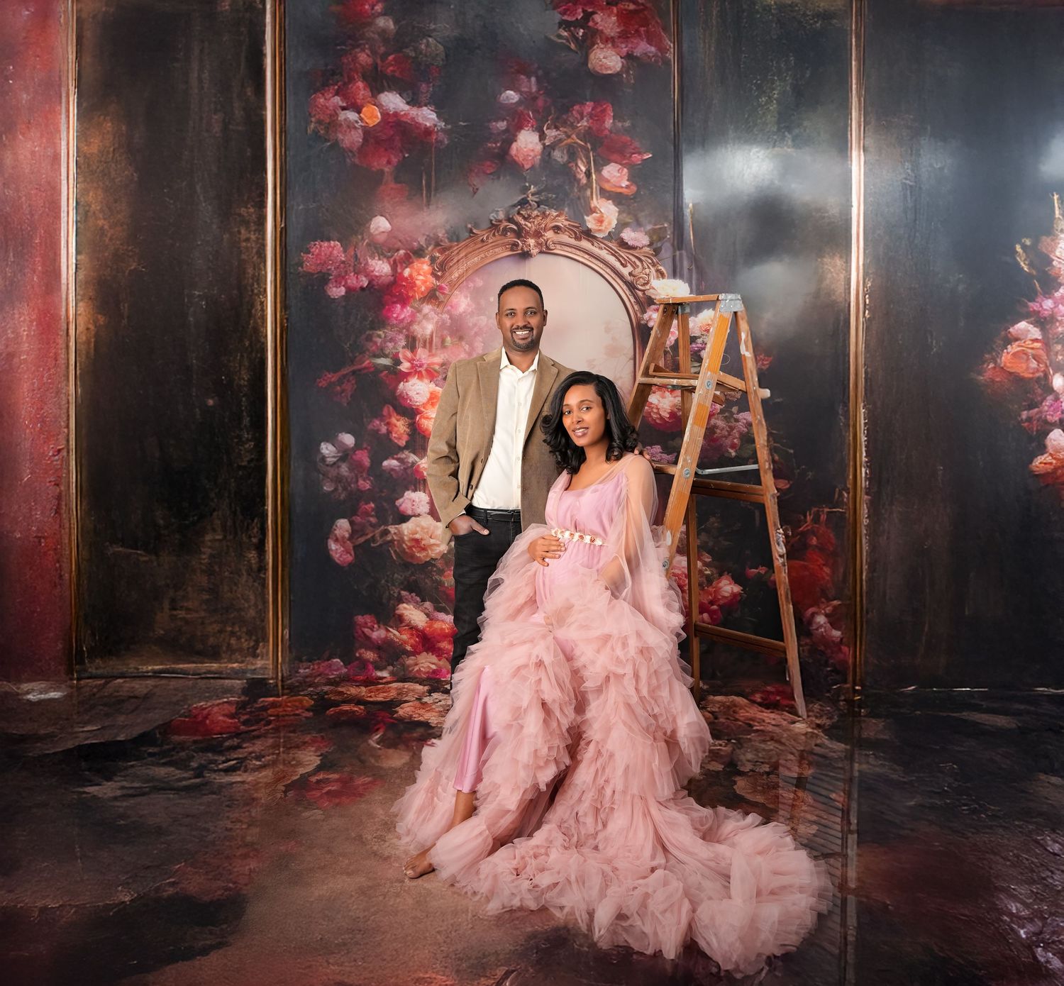 Elegant portrait of a couple in a studio setting with a rustic backdrop adorned with pink cherry blossoms and a wooden ladder.