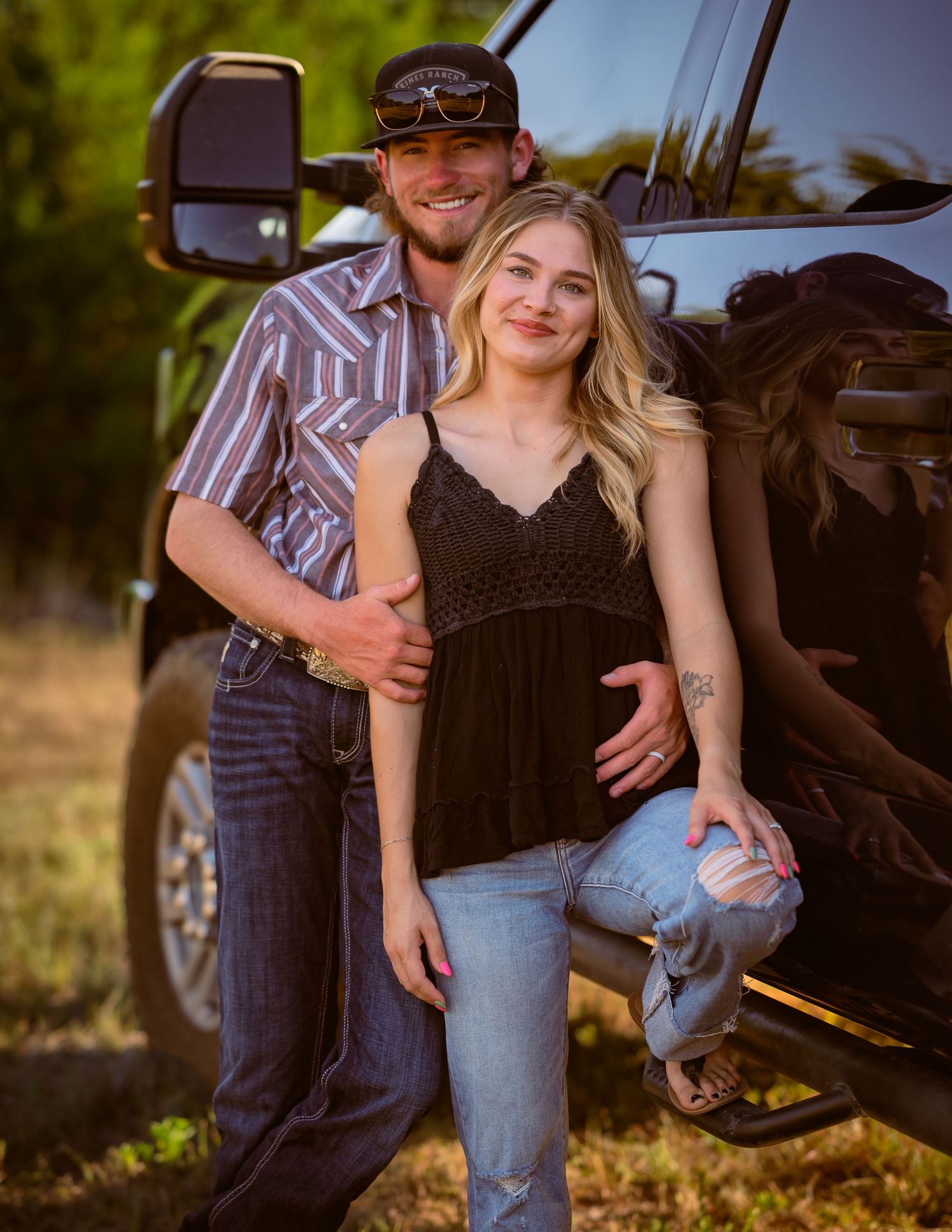 Smiling couple posing beside a black pickup truck in a sunny outdoor setting.