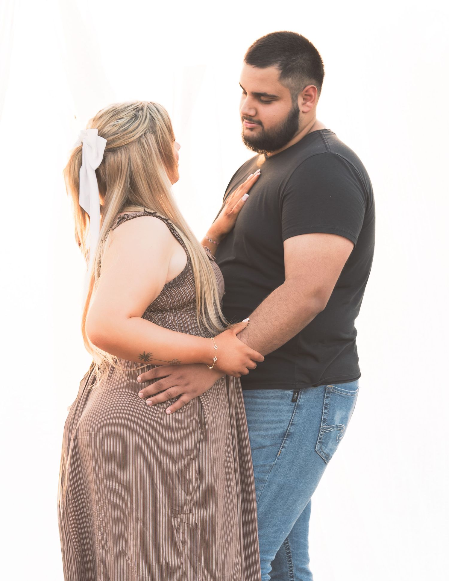 Couple standing close together outdoors, man placing hand on pregnant womans back during photo session.