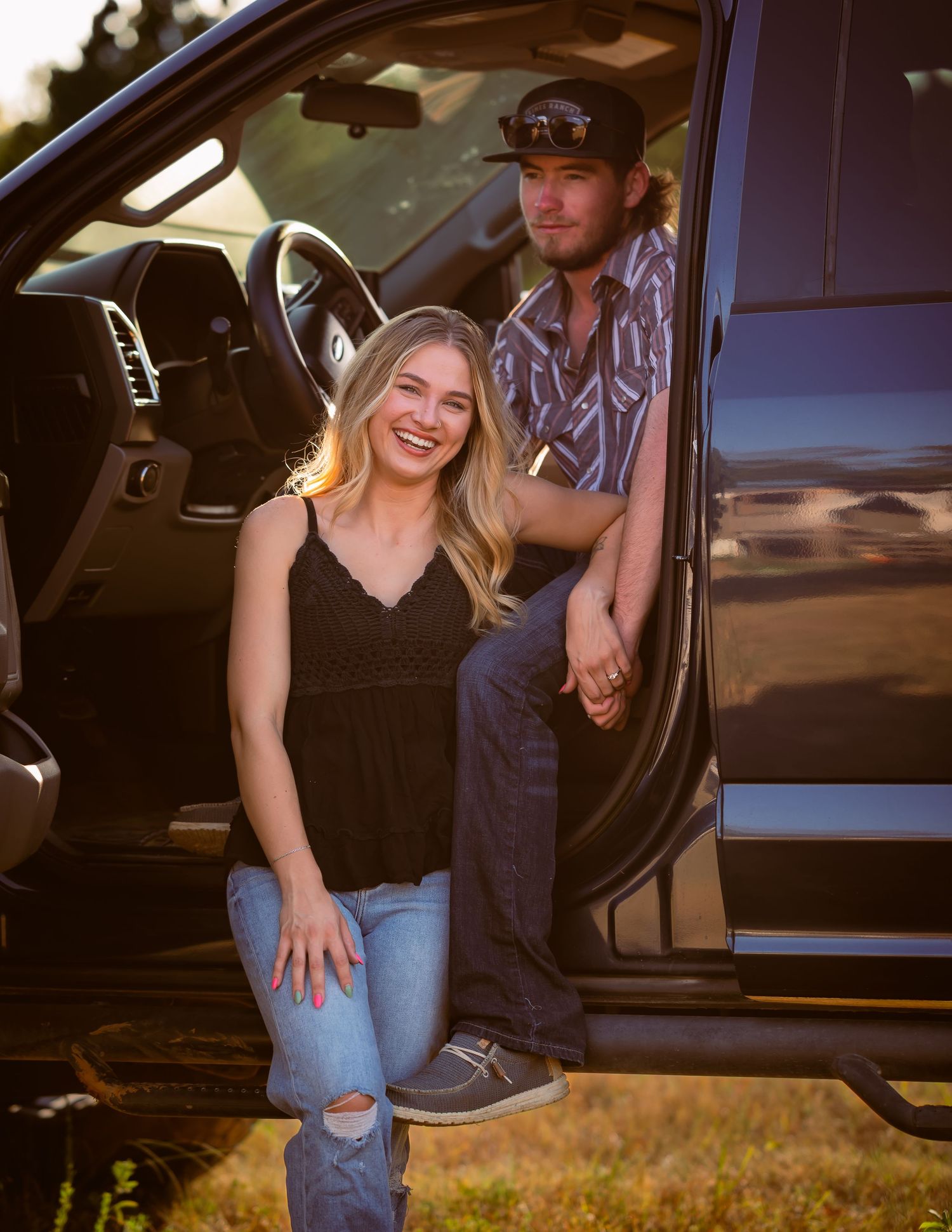 Young woman smiling seated by truck door while man leans in golden light.