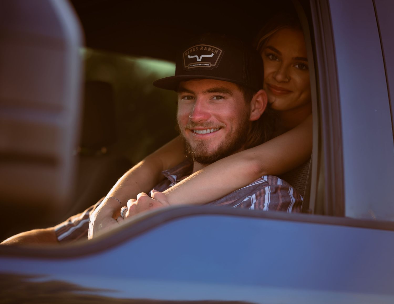 Smiling young man in a cap sitting in a truck with woman behind him.