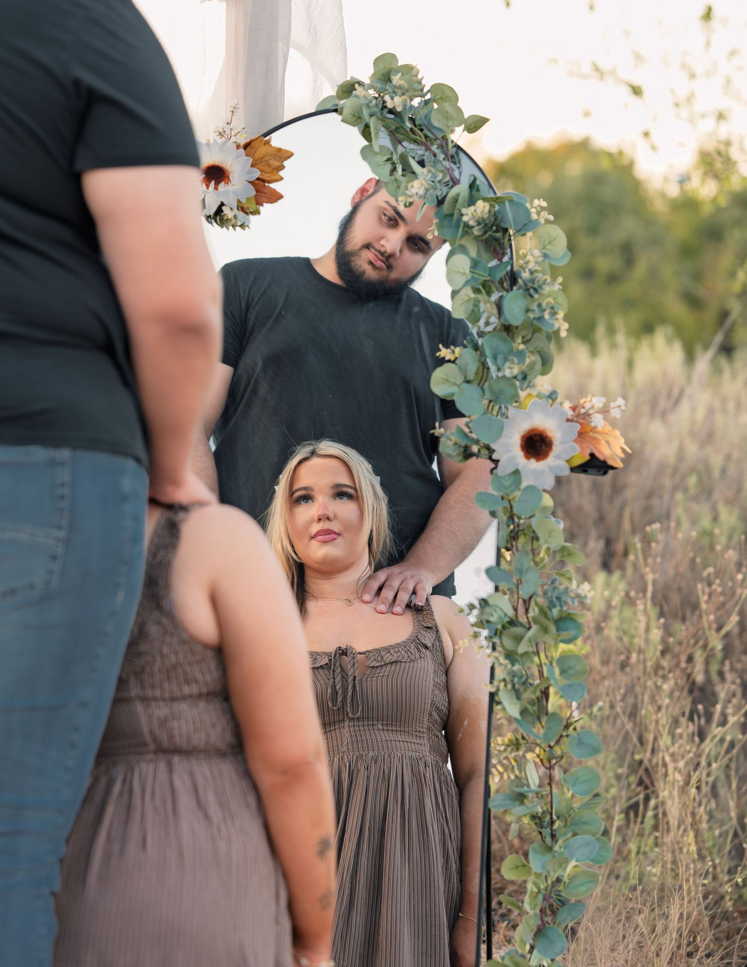 Man gazing at woman through floral arch with sunflowers and eucalyptus during engagement shoot.